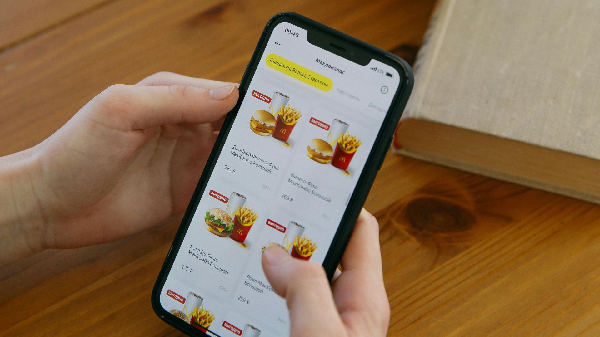 Hands using smartphone to browse food delivery app next to a potted plant.