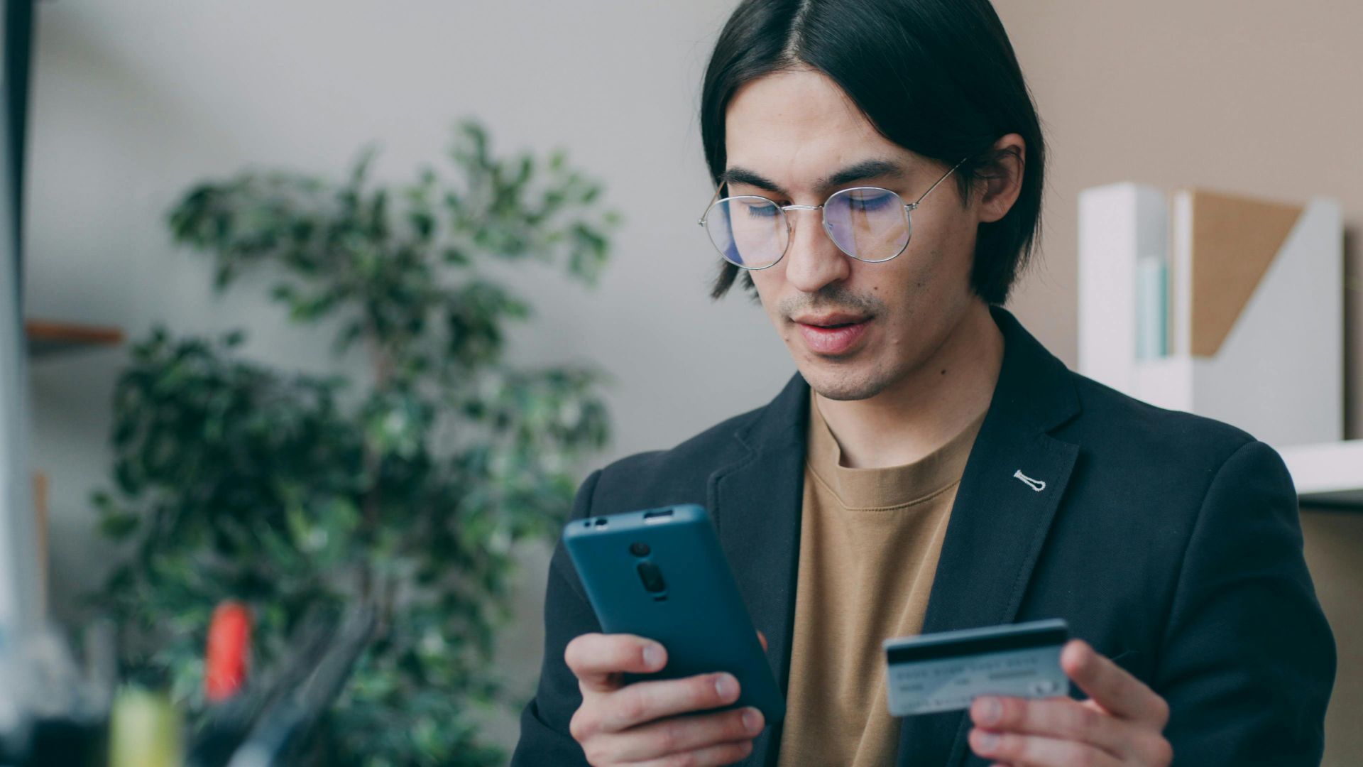 Businessman in office attire using a smartphone and holding a credit card, focusing on online payment process.