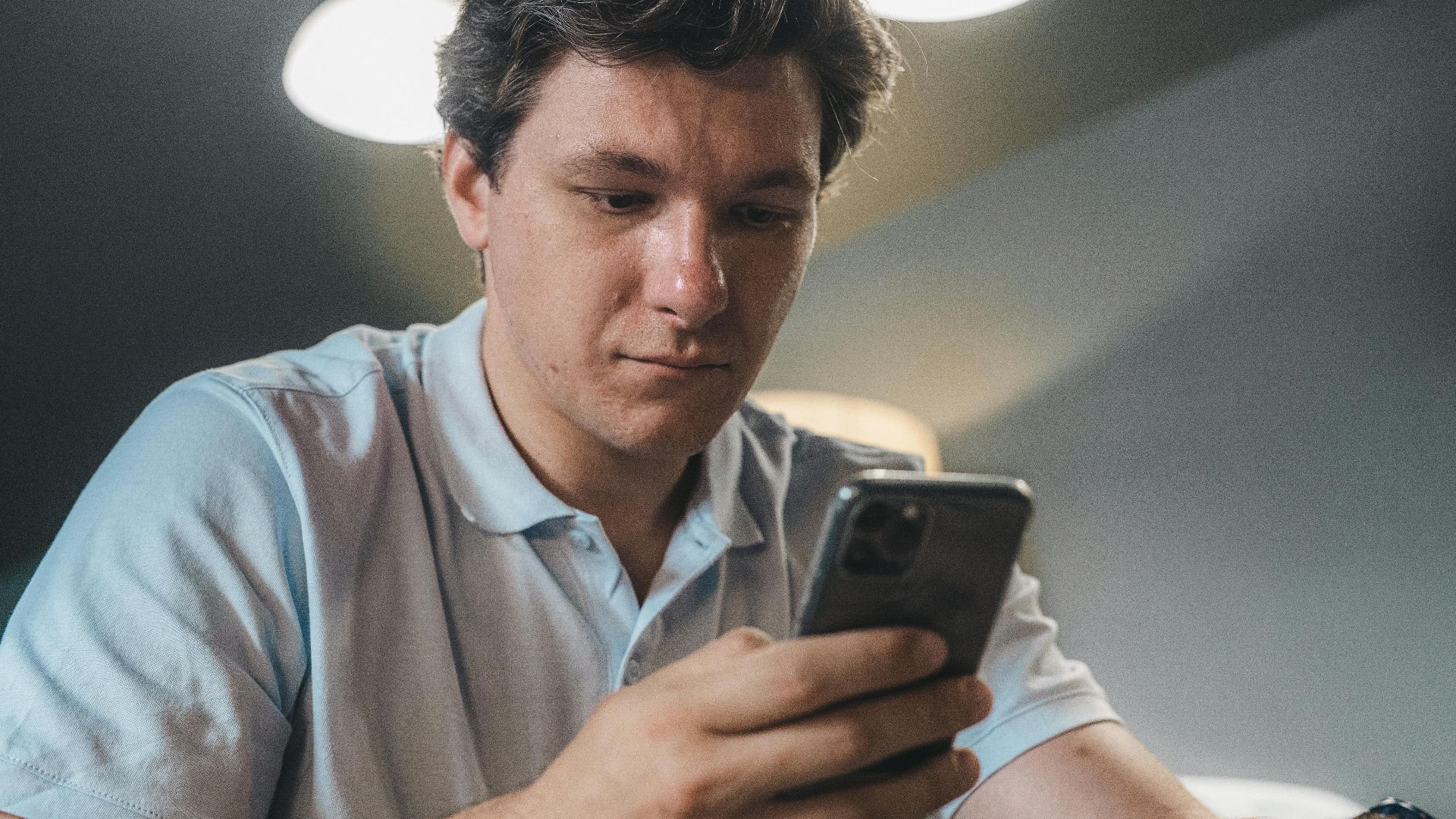 Adult man in casual attire intently using a smartphone indoors, focused and engaged.