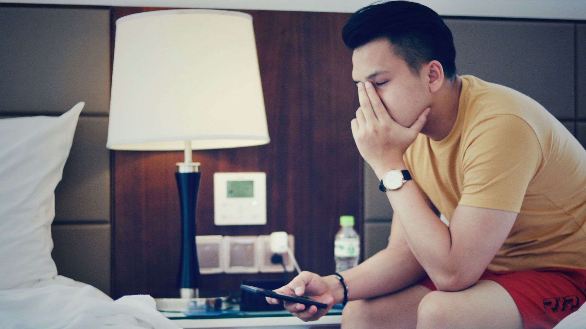 man holding phone and sitting while putting left hand on his face