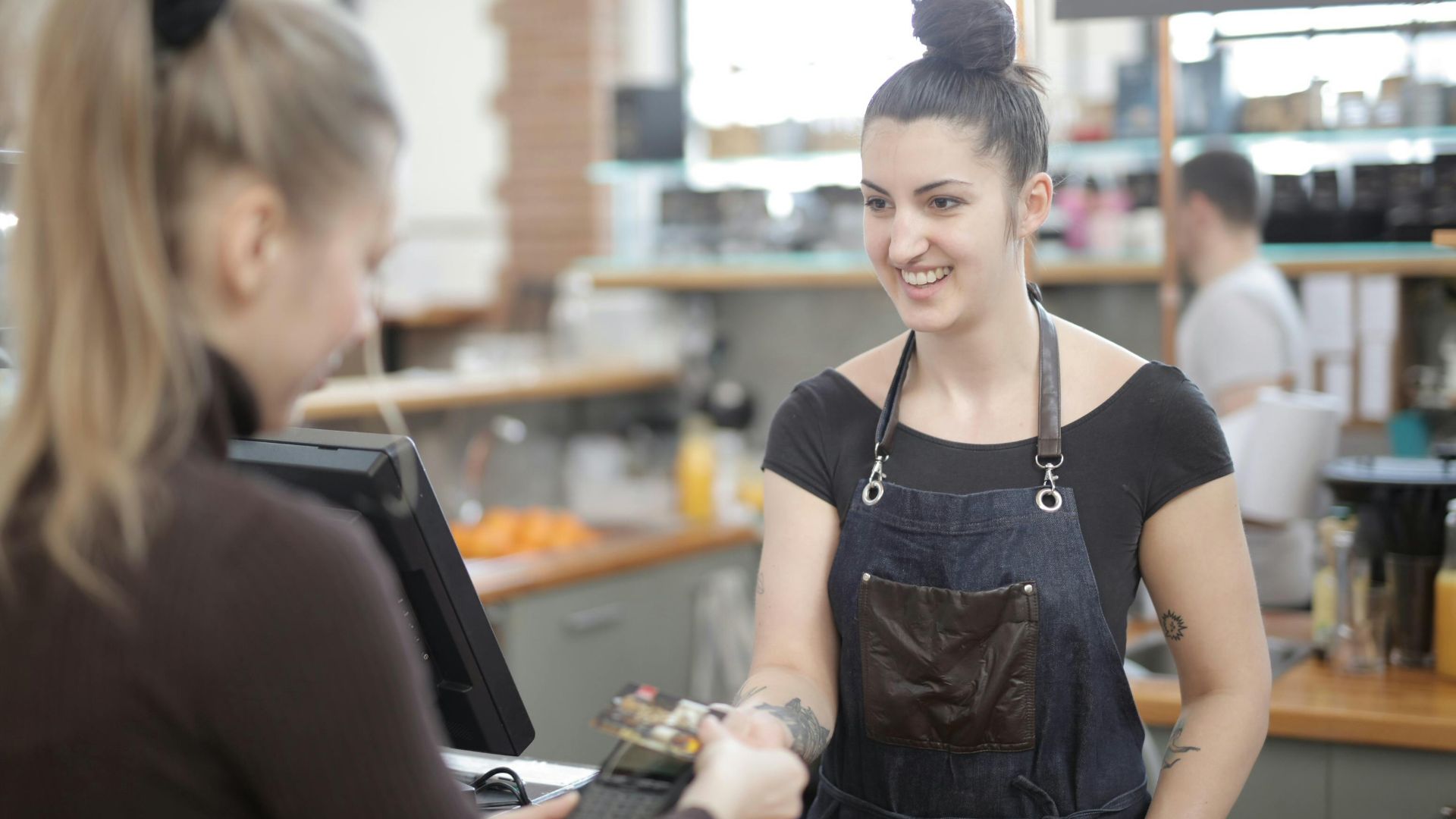 Barista in apron accepting a customer's digital payment in a cozy cafe setting.