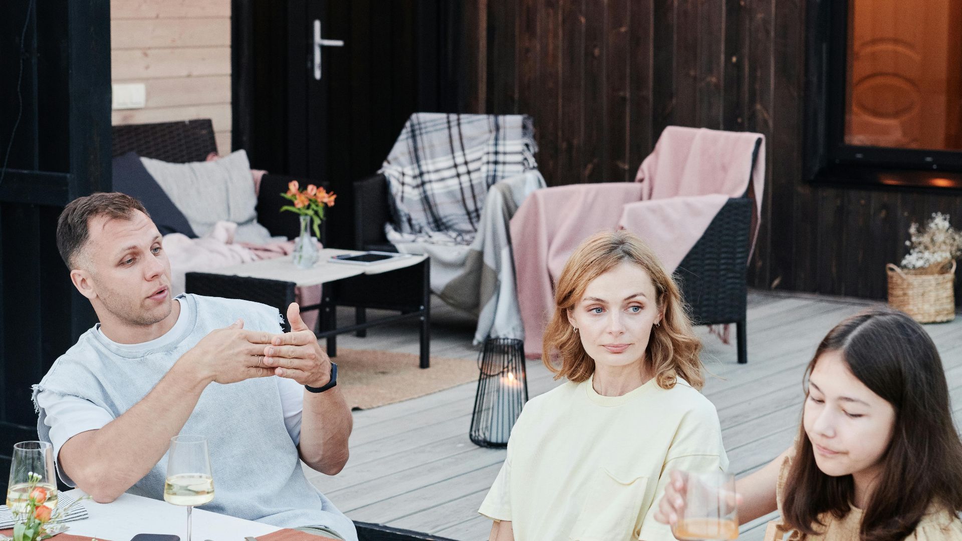 Family enjoying dinner outdoors with candles, food, and drinks on a summer evening.