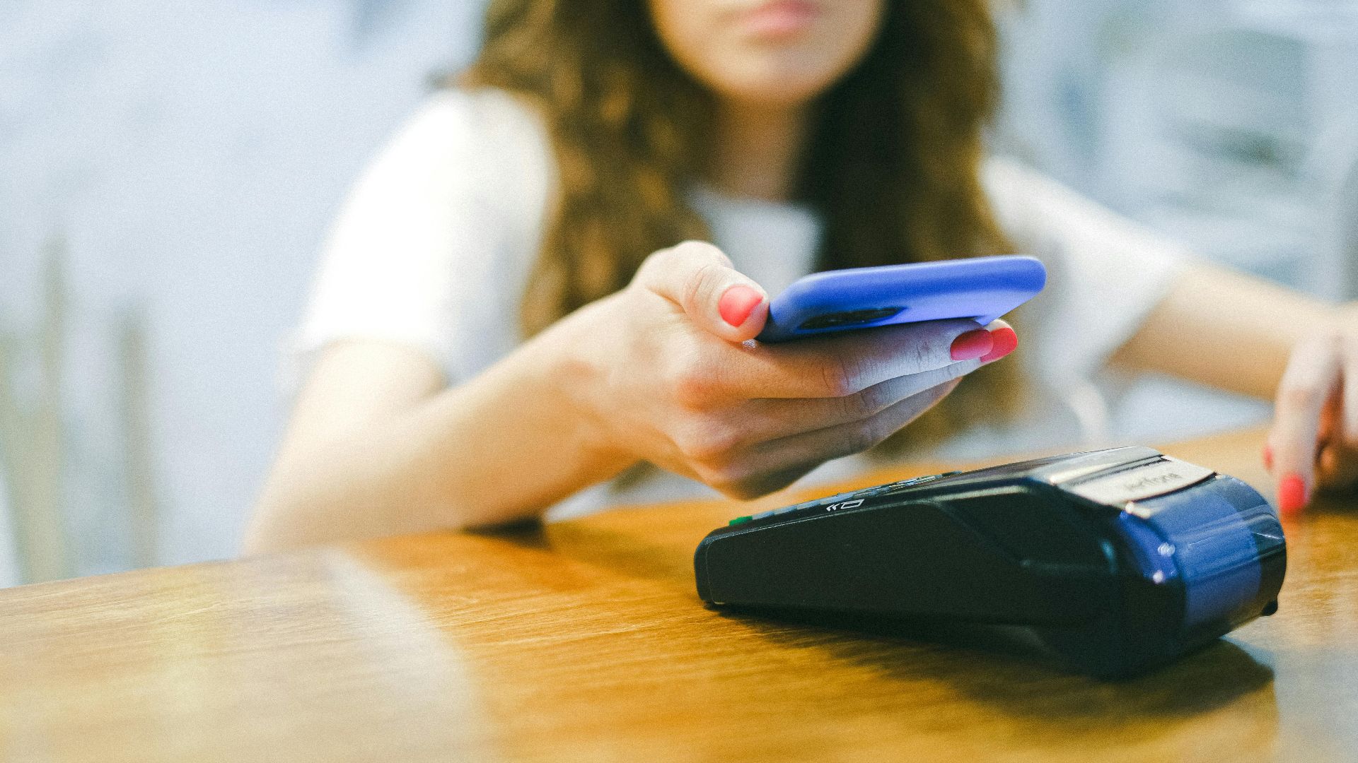 A woman processes a contactless payment using her smartphone at a payment terminal.