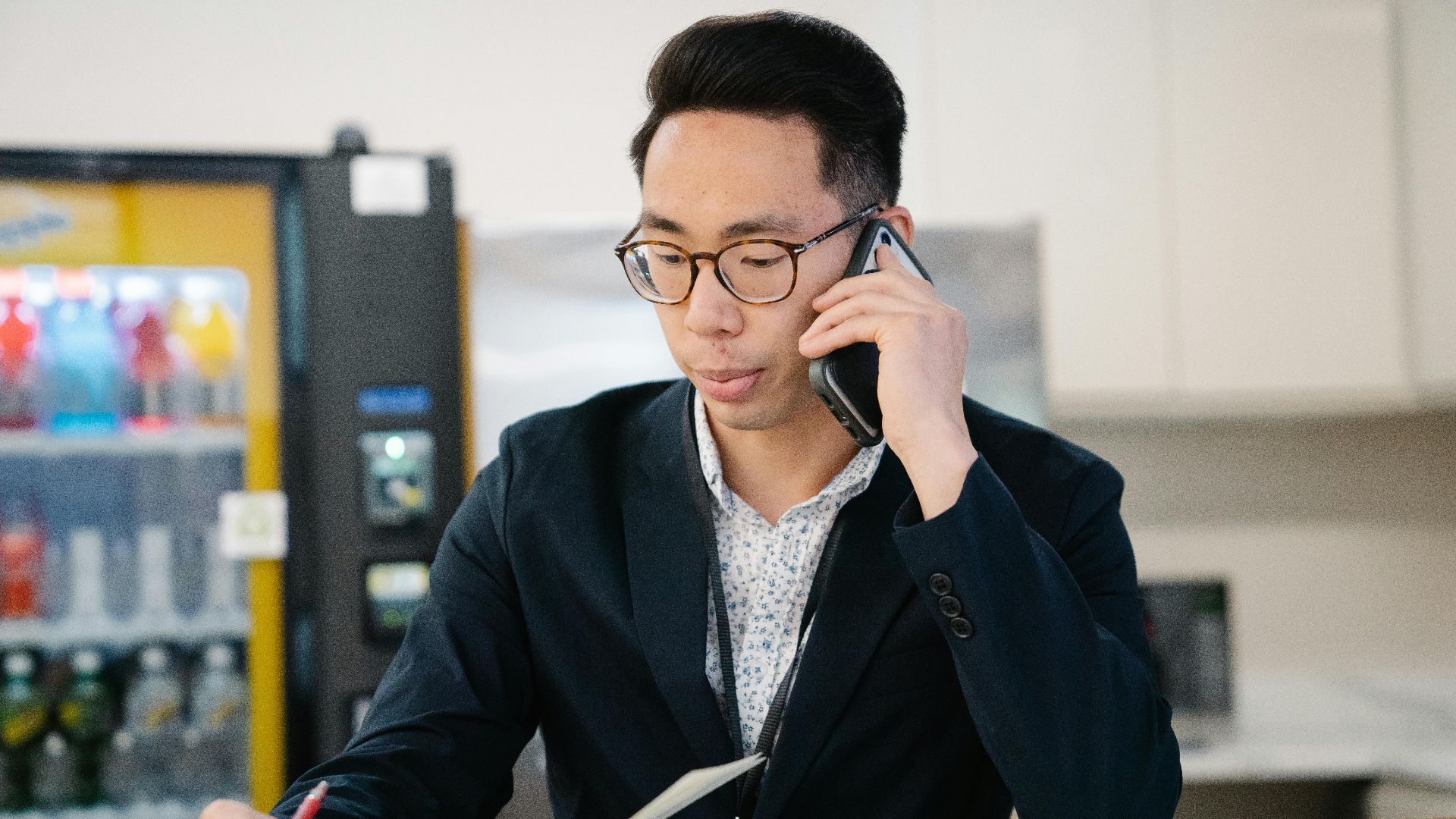 Adult man in a suit talking on mobile phone while taking notes in an office setting.
