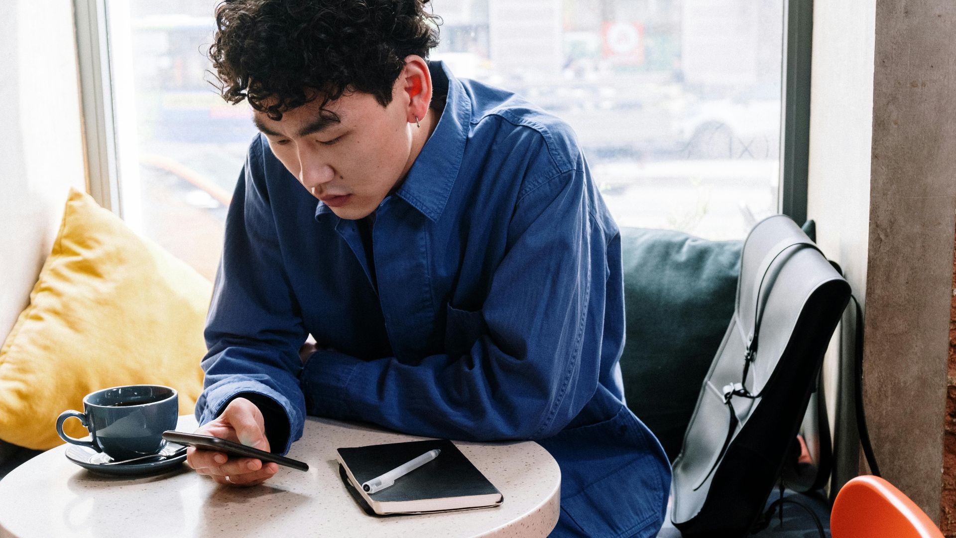 Young man in a cafe using a smartphone, with coffee and notebook on the table.