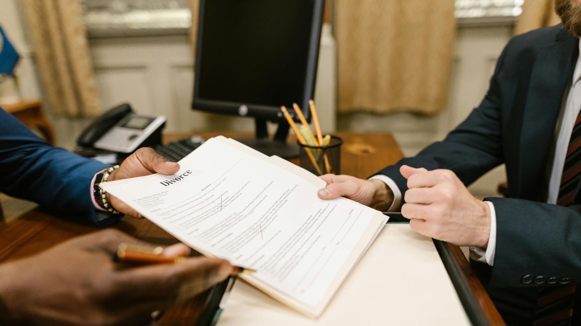 Close-up of hands exchanging divorce documents during legal proceedings in office.