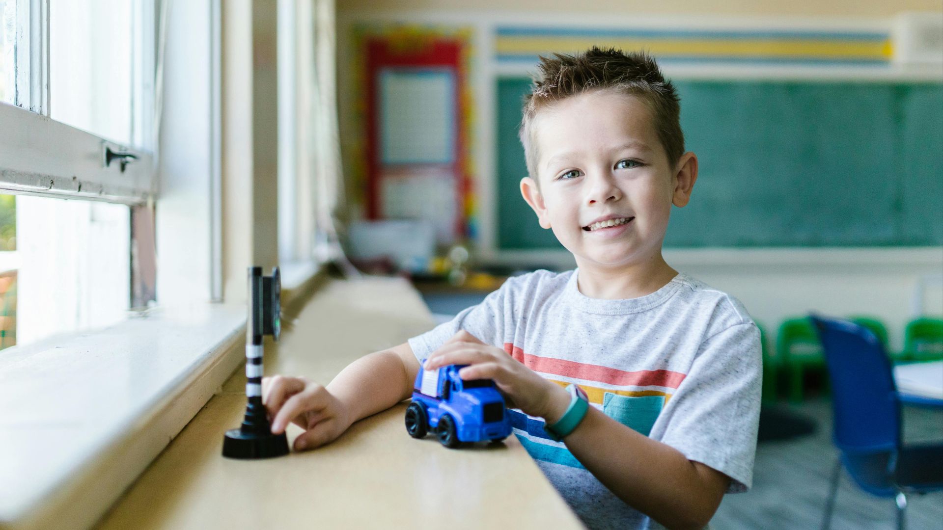 A happy child enjoys playing with a toy car in a bright classroom setting.