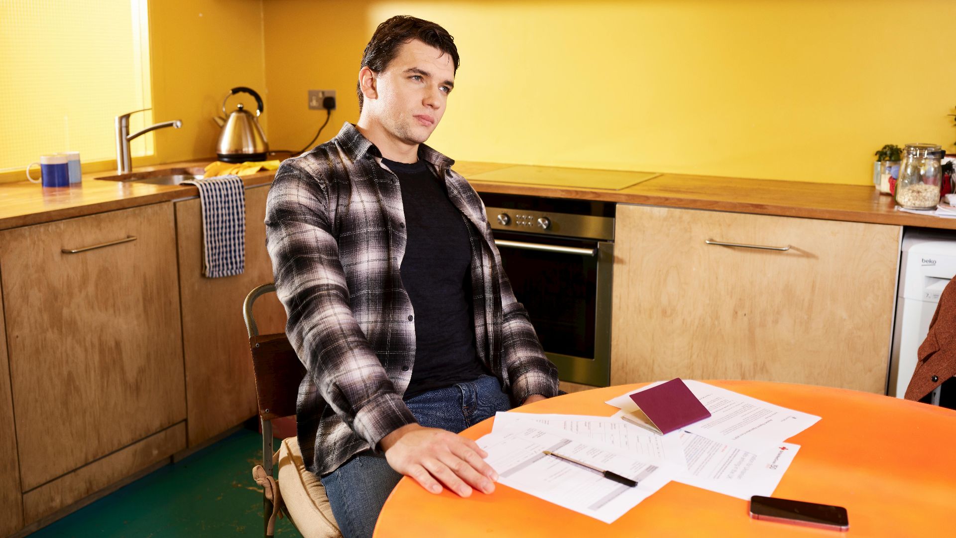 Man sitting at a kitchen table with documents and a passport, contemplating.