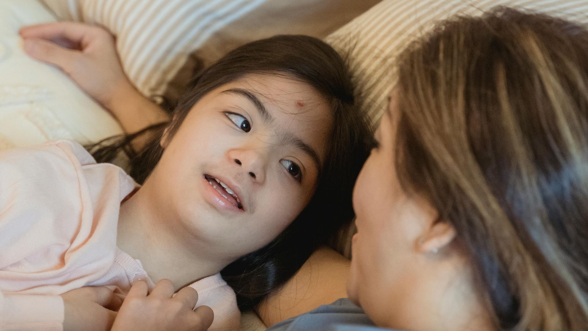 Heartwarming moment between a mother and daughter with Down syndrome enjoying a tender bond in the bedroom.