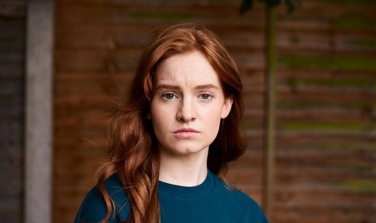 A portrait of a redhead woman with freckles and long hair, showing a neutral expression