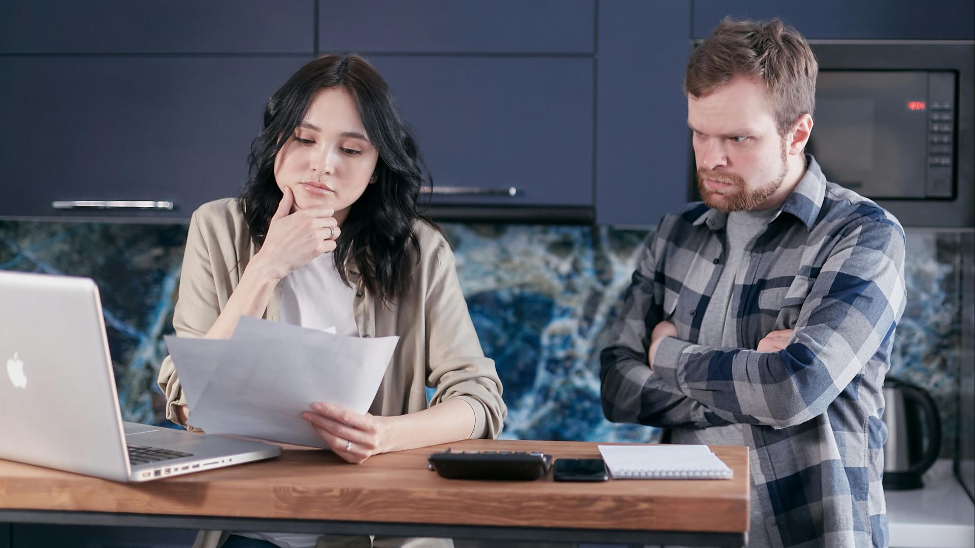 A couple sitting at a kitchen desk reviewing financial documents, using a laptop.