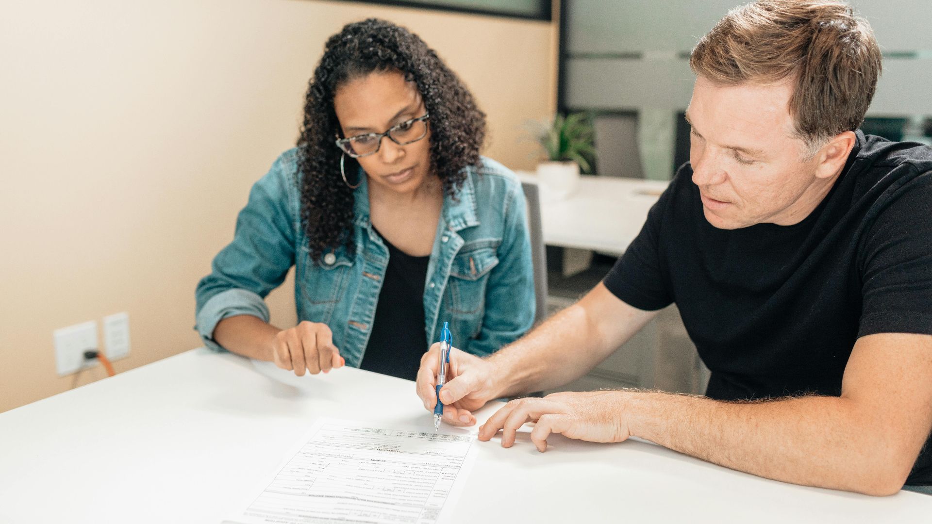 A couple working together to sign important legal documents at a desk in an office setting.