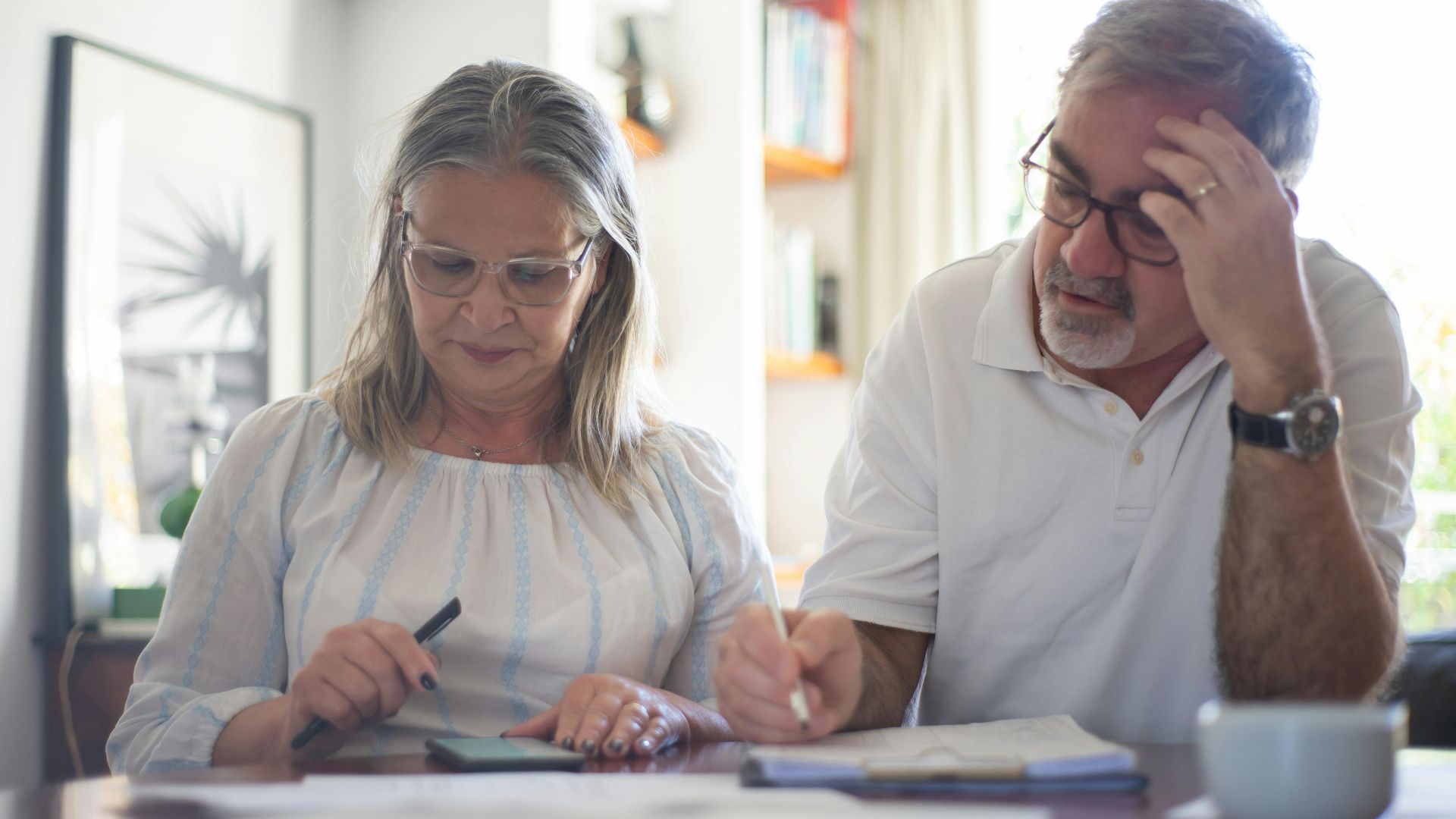Senior couple calculating expenses at home office desk with documents and notes.