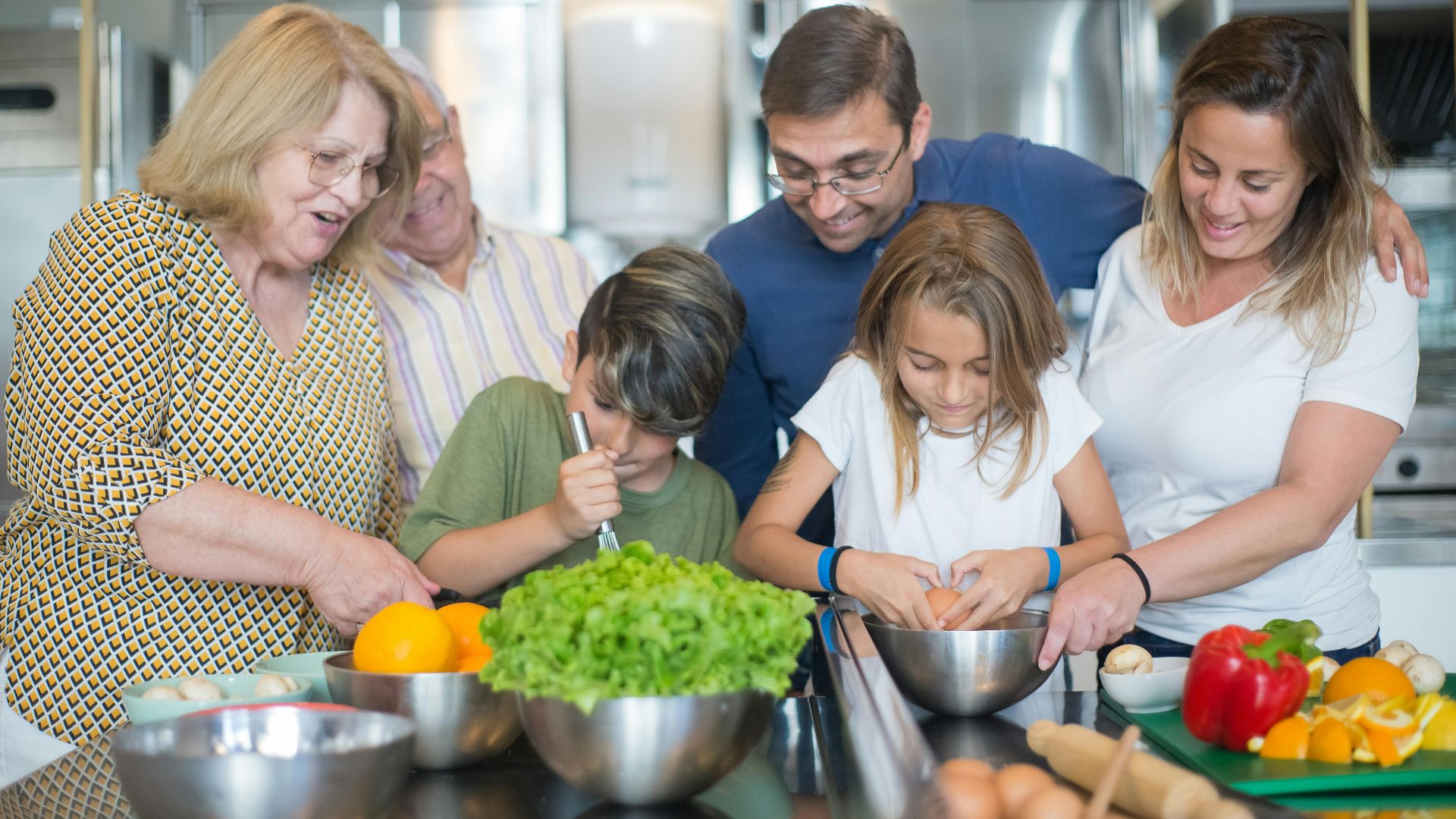 Family of various ages gathers in kitchen to cook meal together, showcasing culinary togetherness.