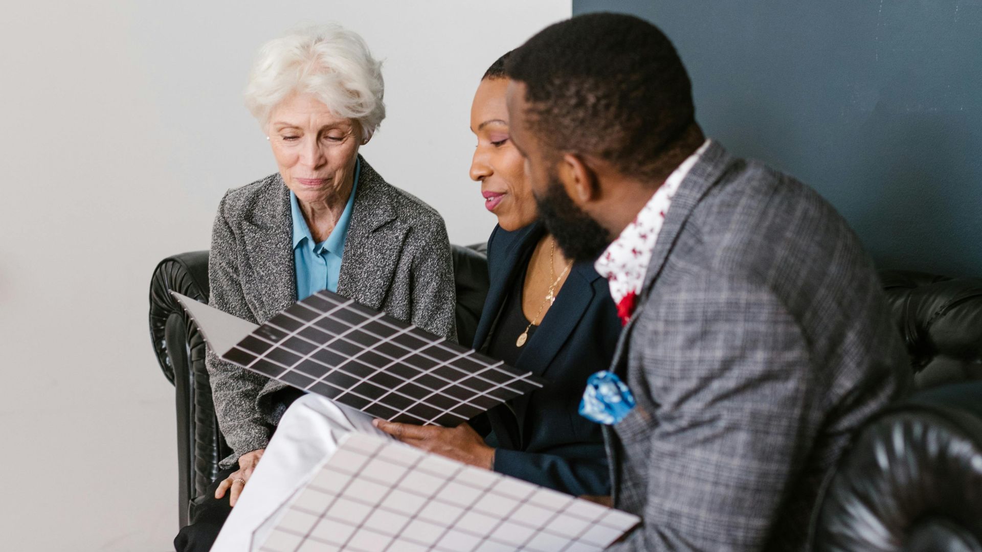 Three people of different ethnicities discuss business strategy, reviewing documents in an office setting.