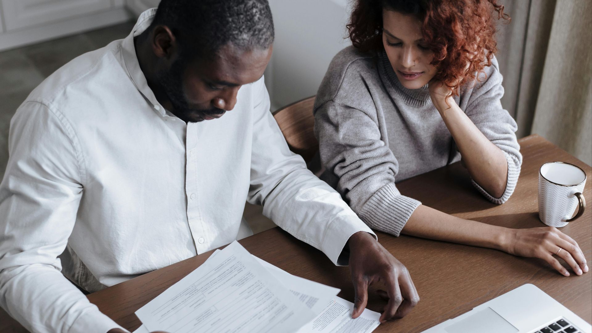 A couple reviews important documents together at a home desk with a laptop.