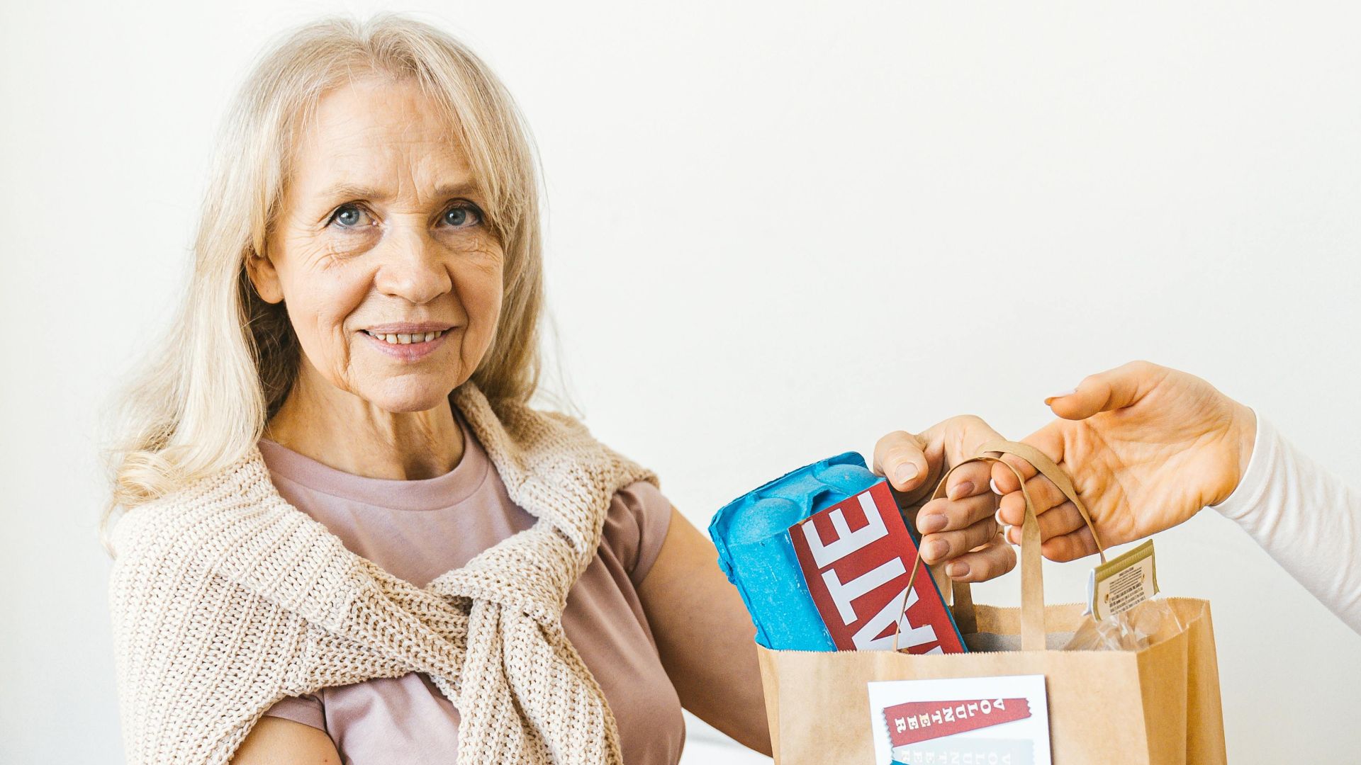 Senior woman smiling and receiving a grocery bag indoors, highlighting community assistance.