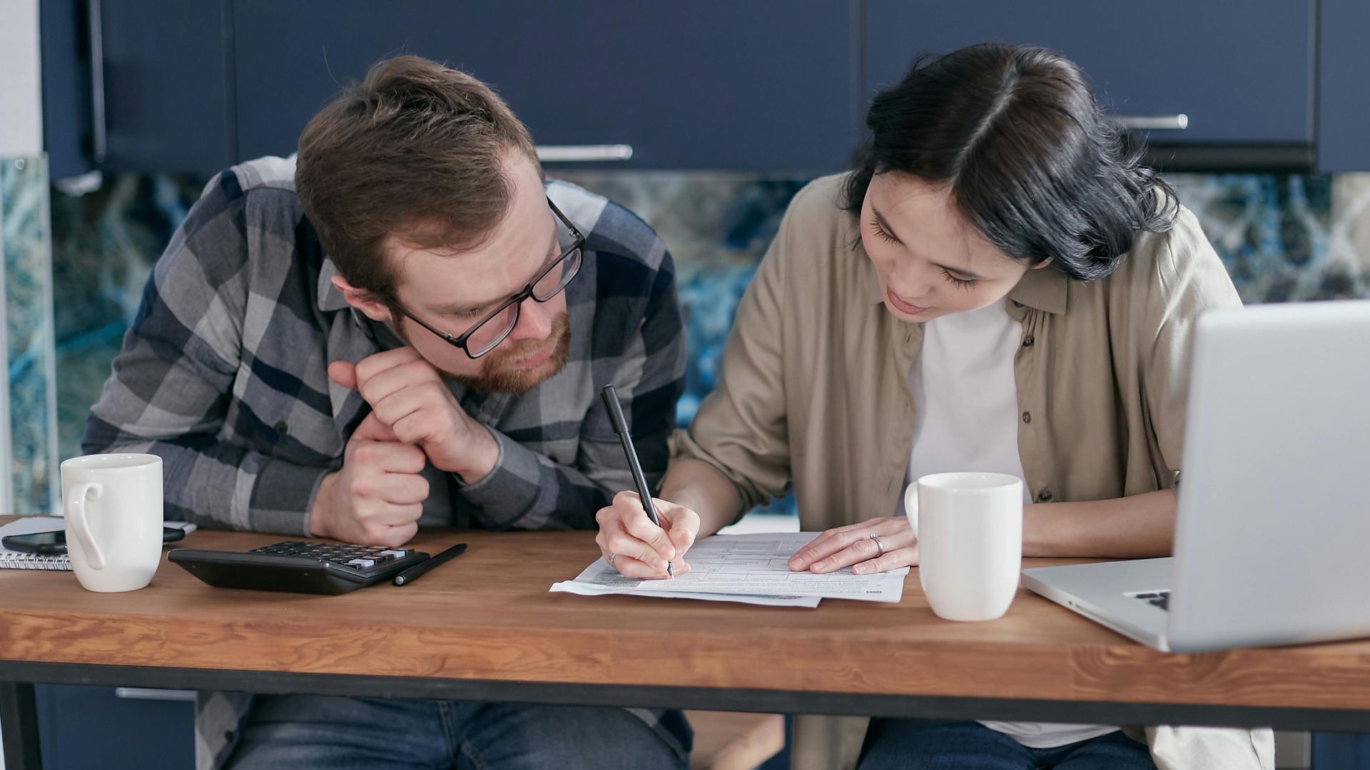 Couple reviewing financial documents together at a kitchen table with a laptop and calculator.