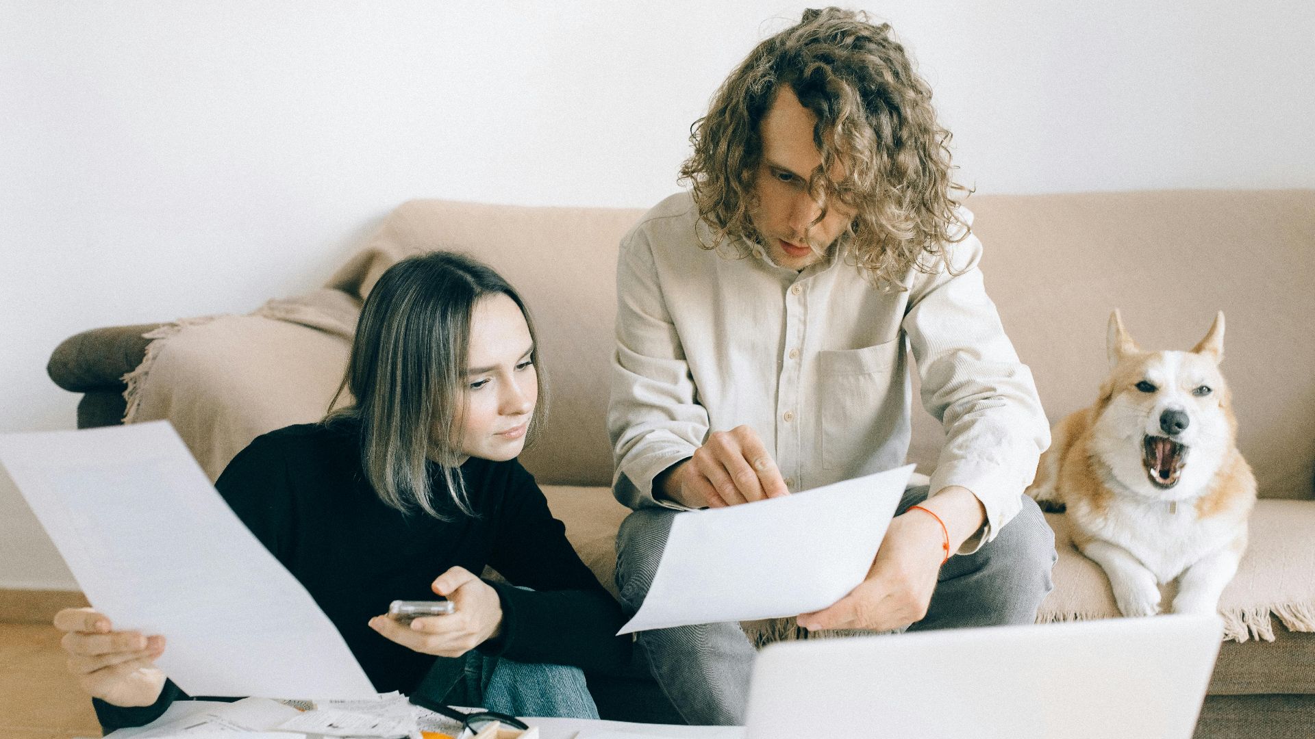 A couple working remotely at home with documents and a dog on the sofa.