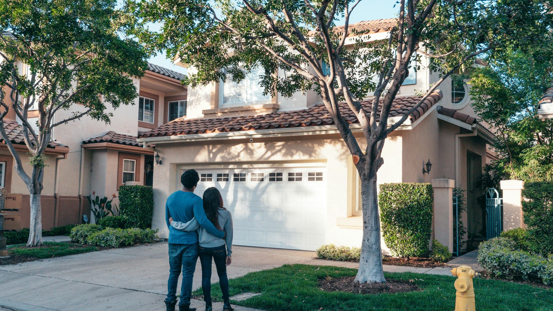 Couple hugging outside their newly purchased suburban home, showcasing togetherness and new beginnings.