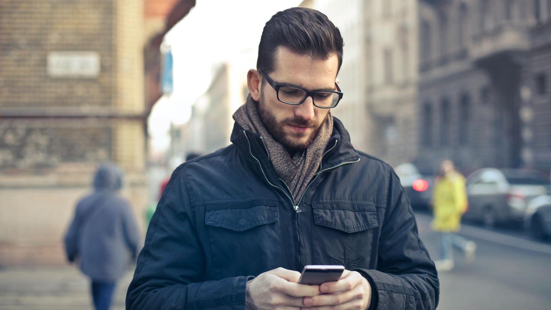 Adult man with glasses using a smartphone on a city street in Budapest, Hungary.