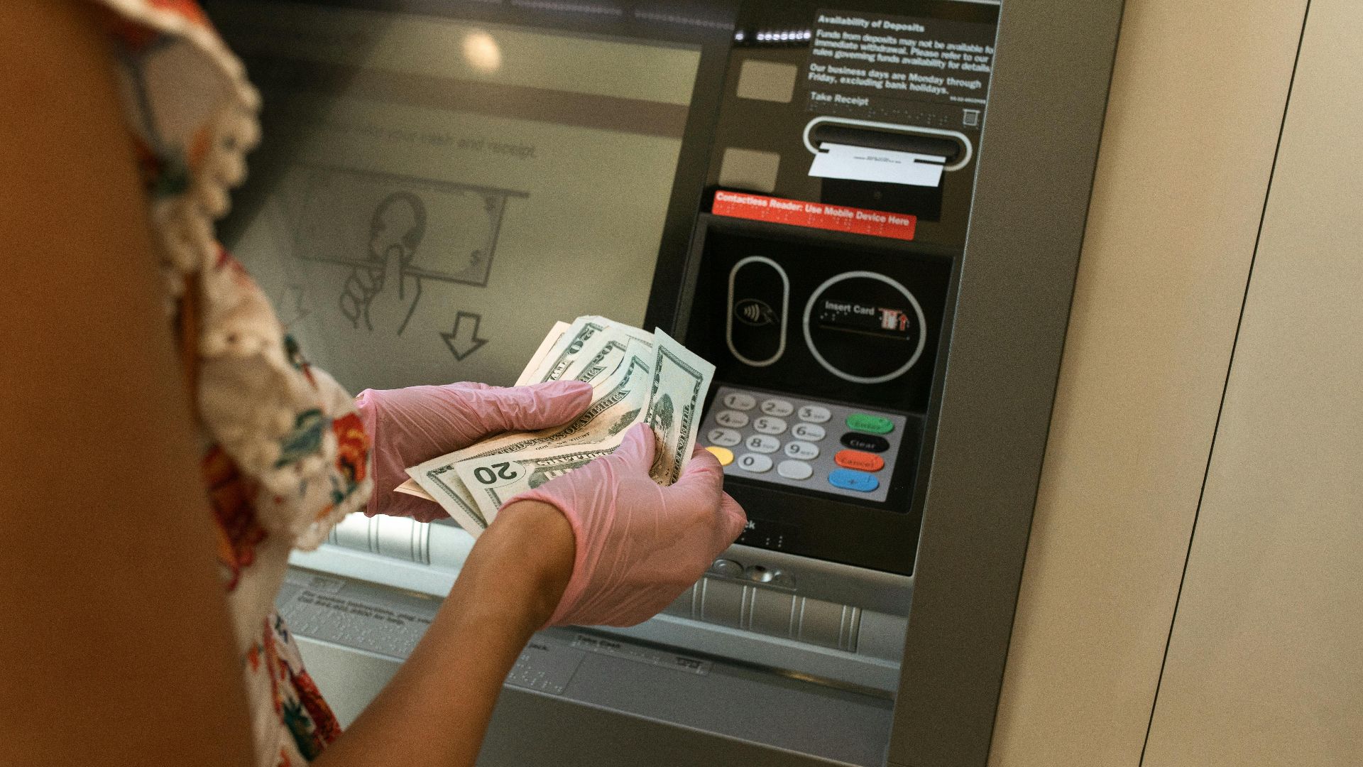 A person wearing gloves withdraws cash from an ATM, ensuring hygiene.