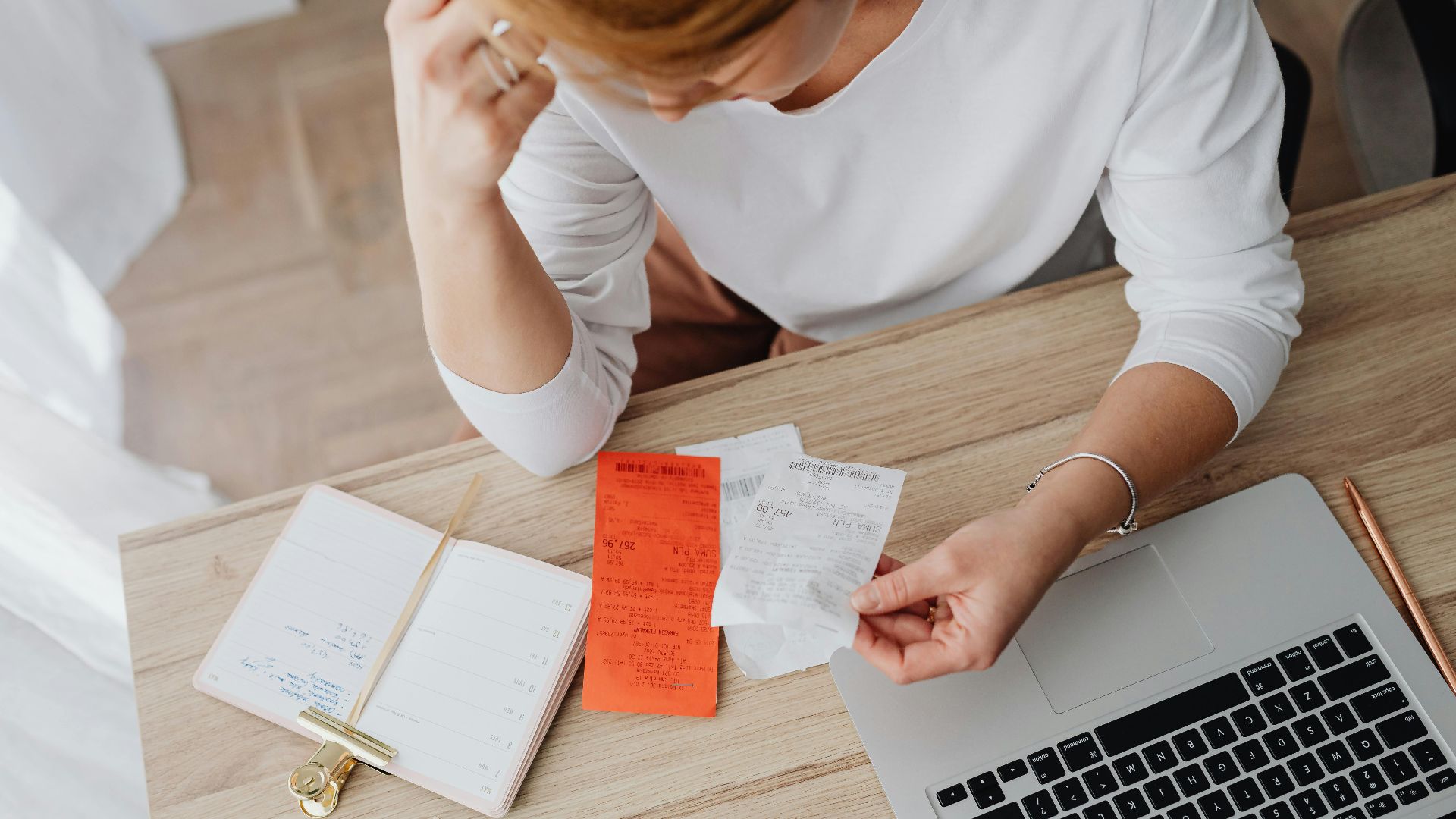 Woman reviewing receipts and planning budget using a laptop and notebook at home to manage expenses.