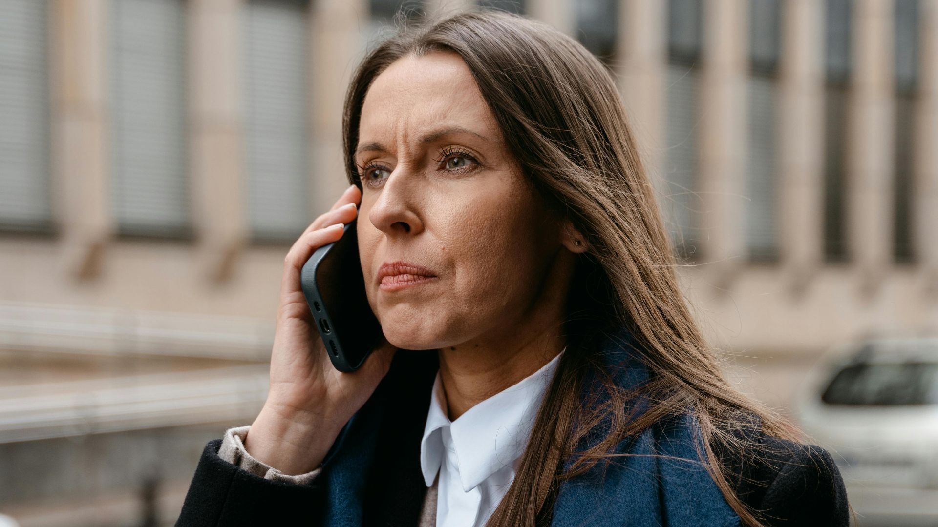 Confident woman in business attire talking on phone while walking in urban setting.