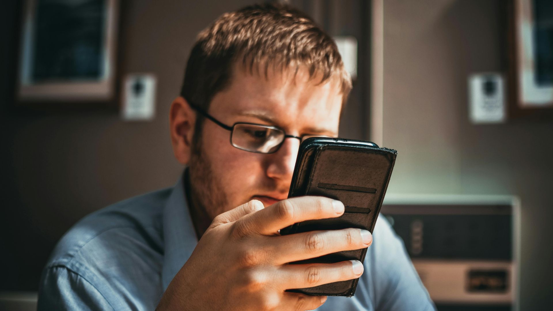 Serious businessman wearing glasses focused on smartphone in a modern office setting.