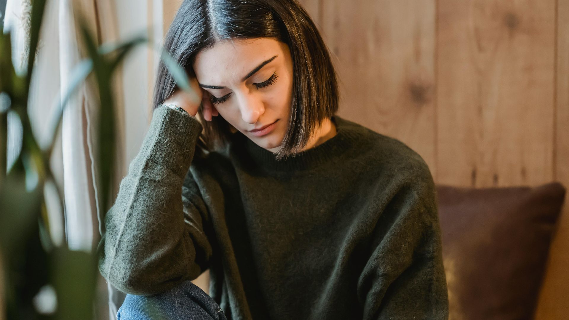 Tired female with closed eyes leaning on hand while having break and nap near window