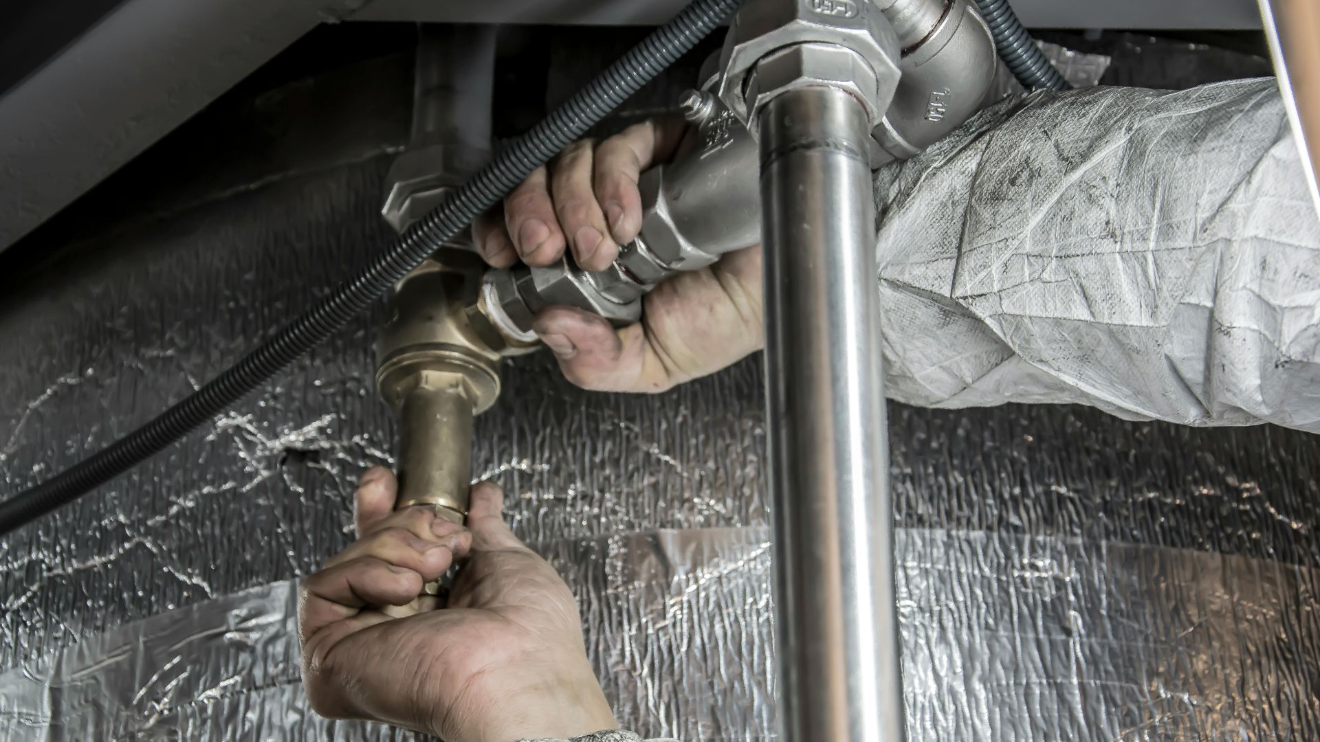Close-up of a plumber's hands installing steel pipes indoors, showcasing skilled manual work.