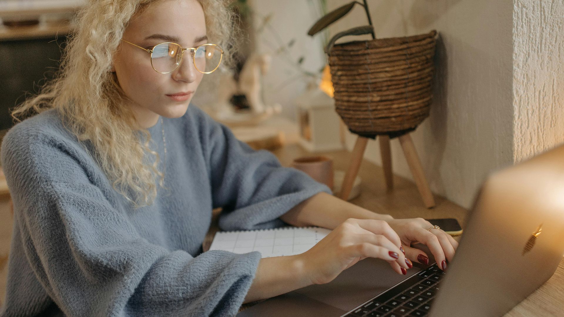 Focused young woman with curly hair working on her laptop in a cozy home office setting.