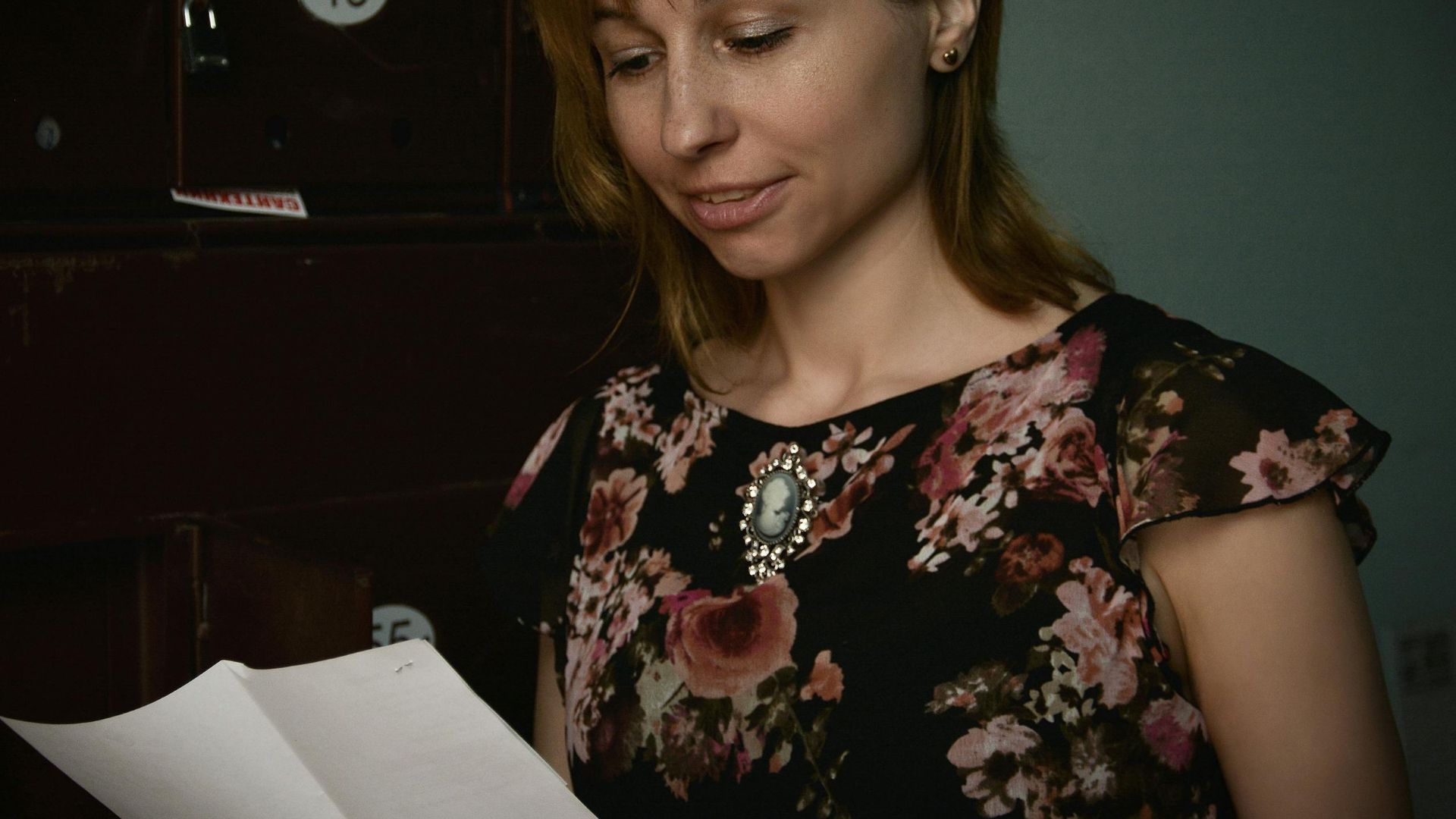 Woman reading mail from mailbox in a floral blouse. Indoor setting.