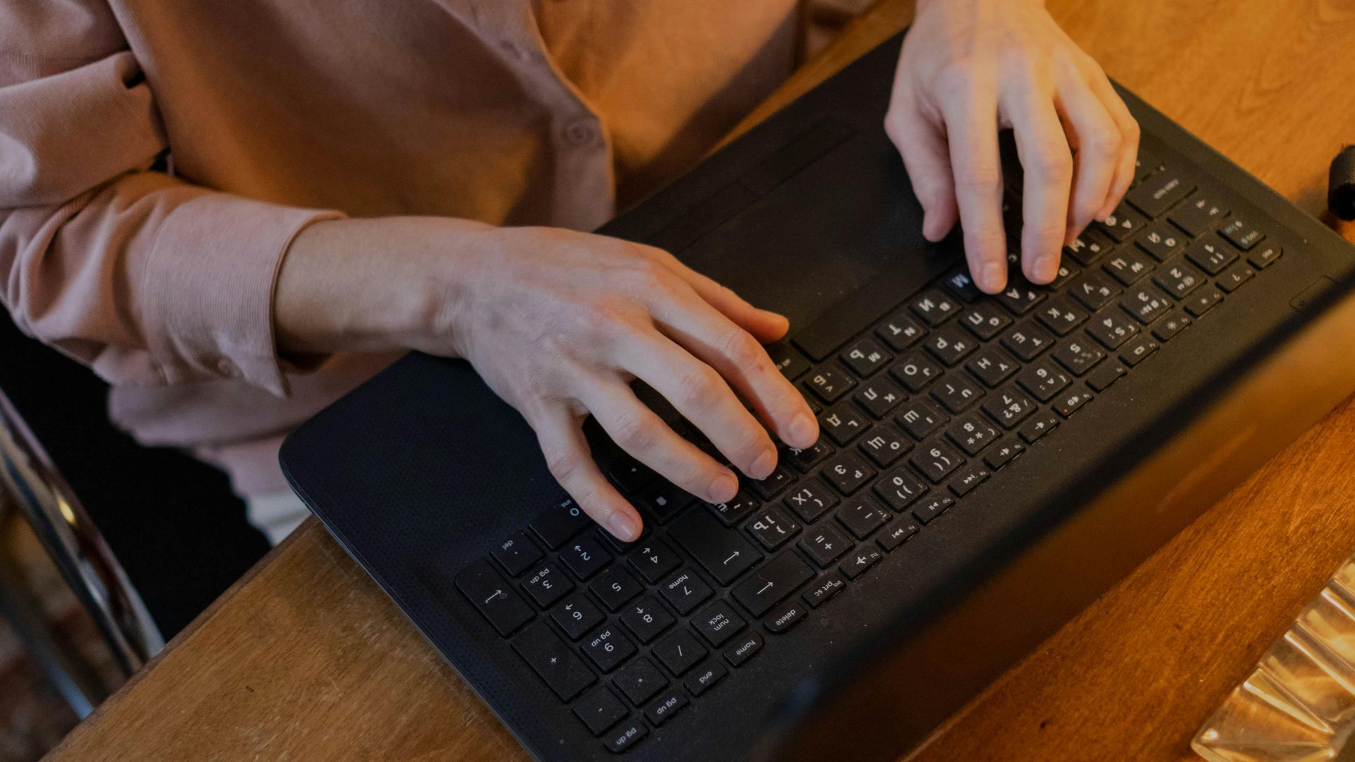 A woman typing on a laptop at a wooden table inside a cozy room, focusing on remote work.