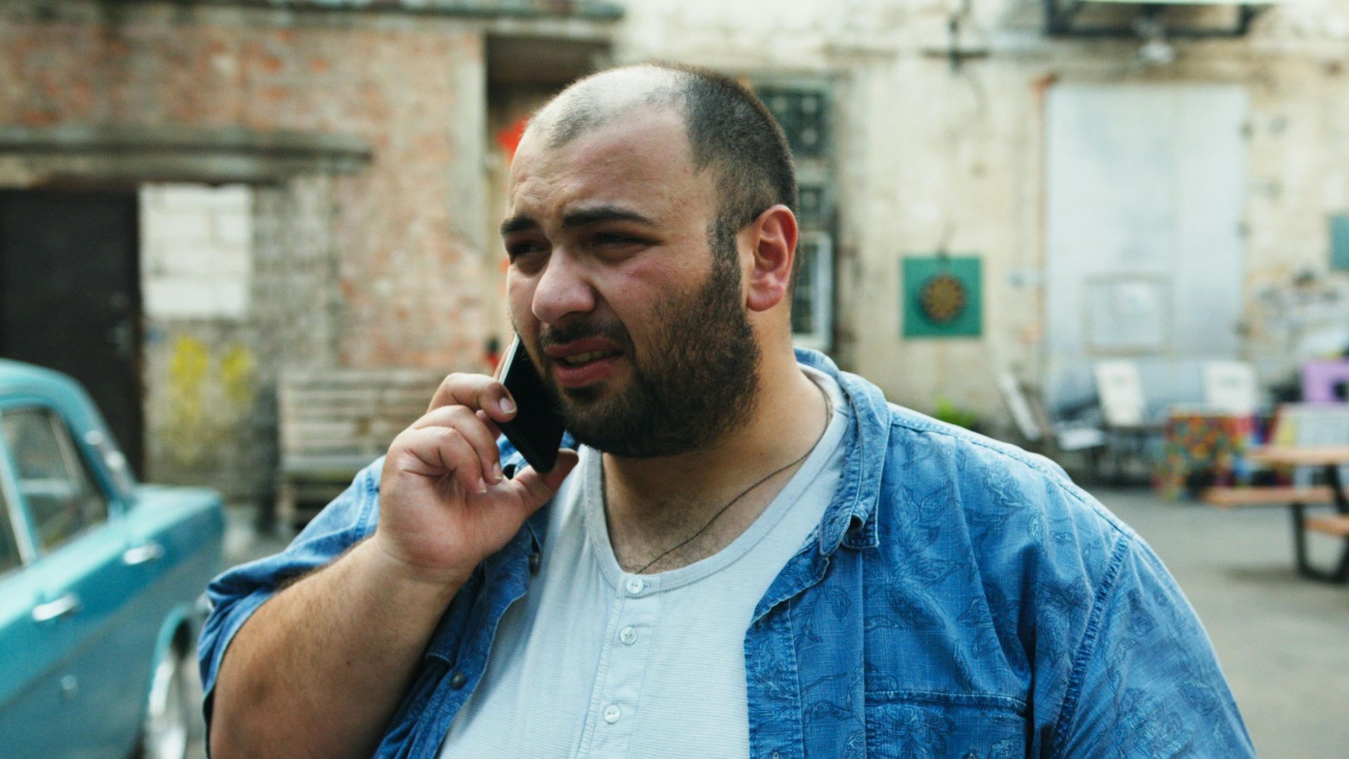 Bearded man with denim shirt using smartphone outside in urban setting.