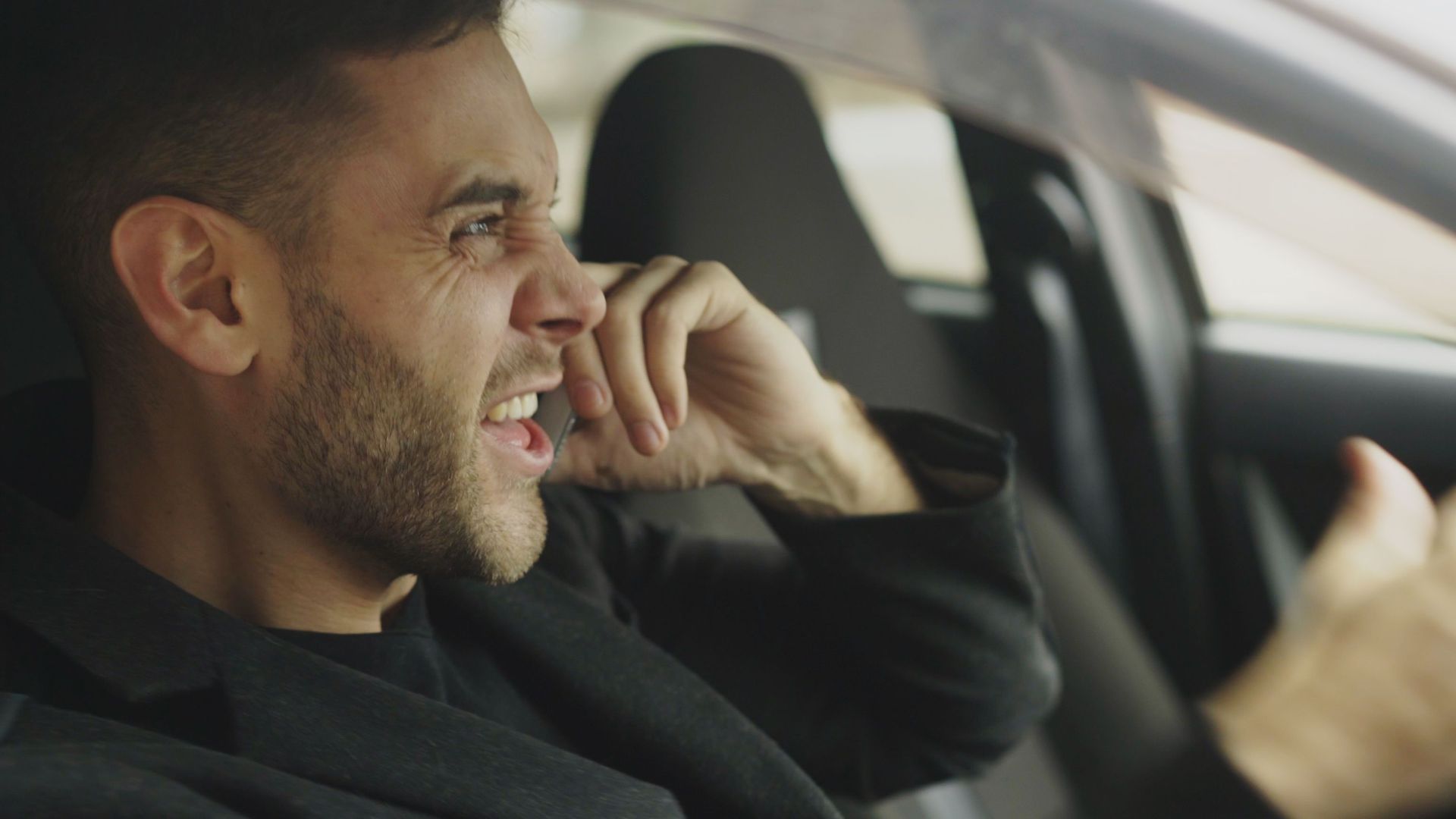 An adult man expressing frustration while on the phone inside a car.
