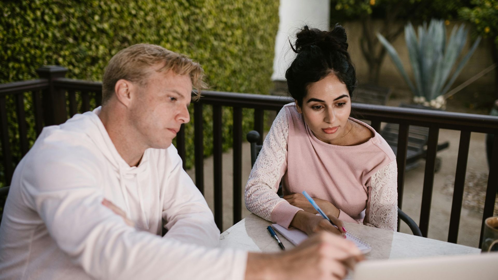 A man and woman engaged in online learning outdoors, collaborating on a laptop.