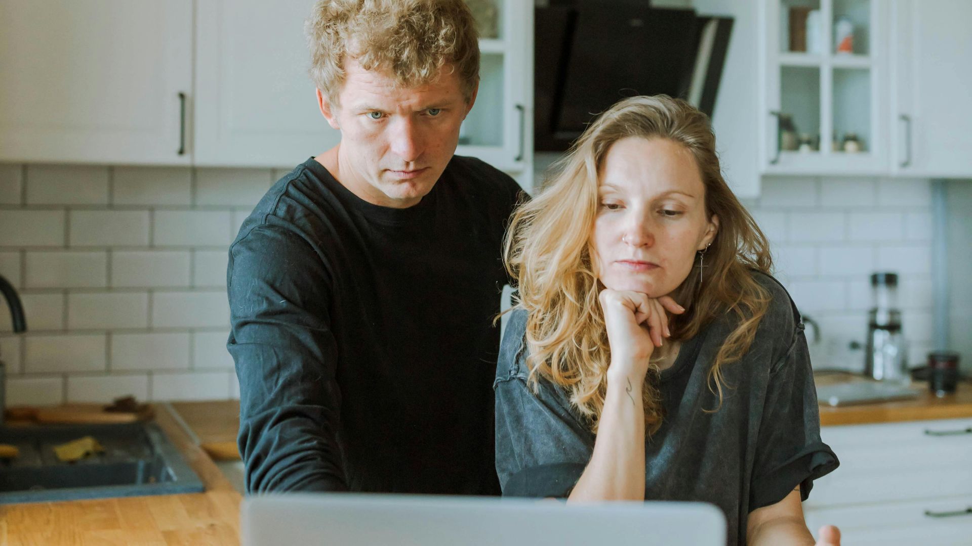 Man and woman focused on laptop work in a bright, modern kitchen setting.