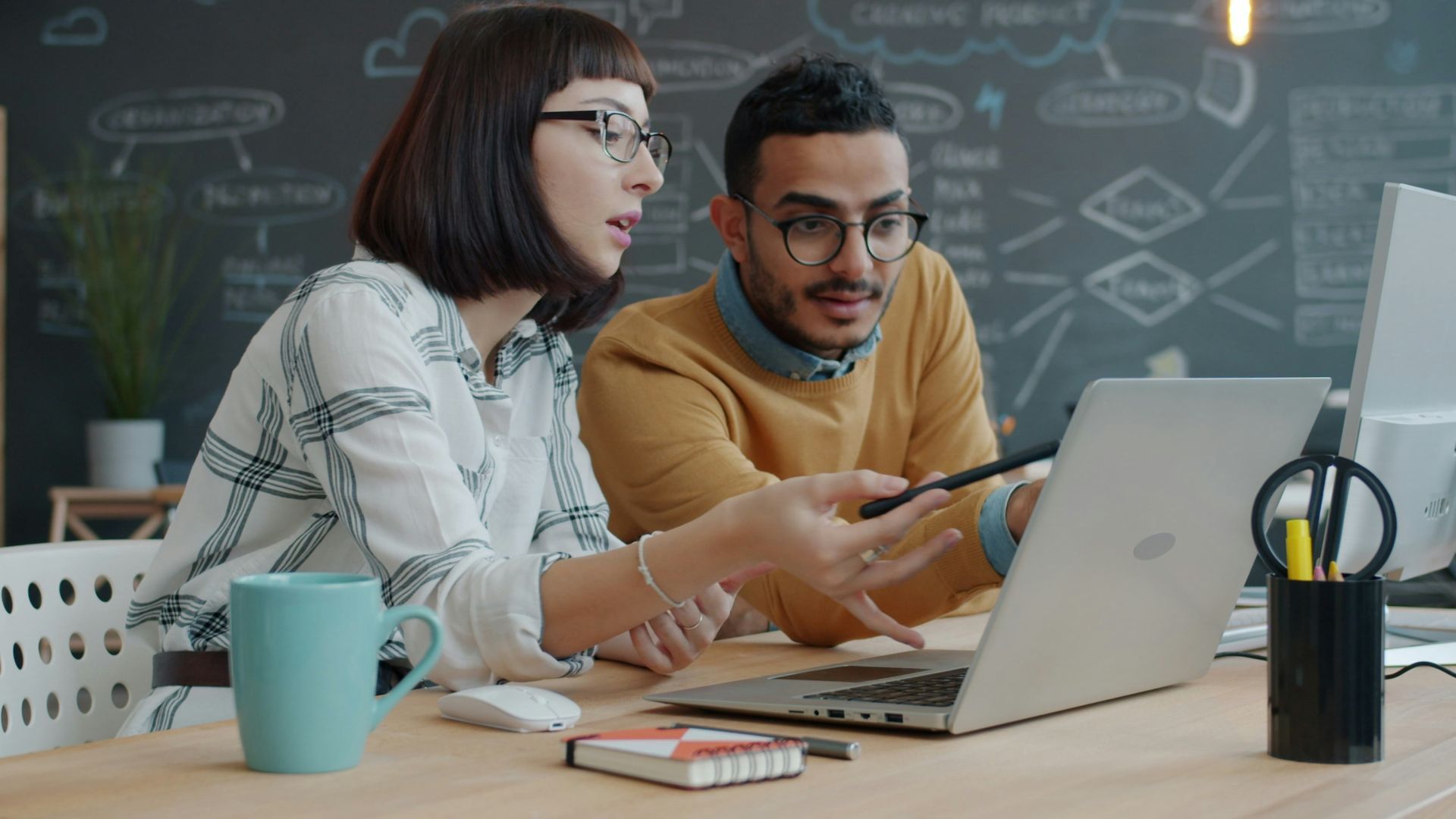 Two colleagues collaborating on a laptop at a desk.