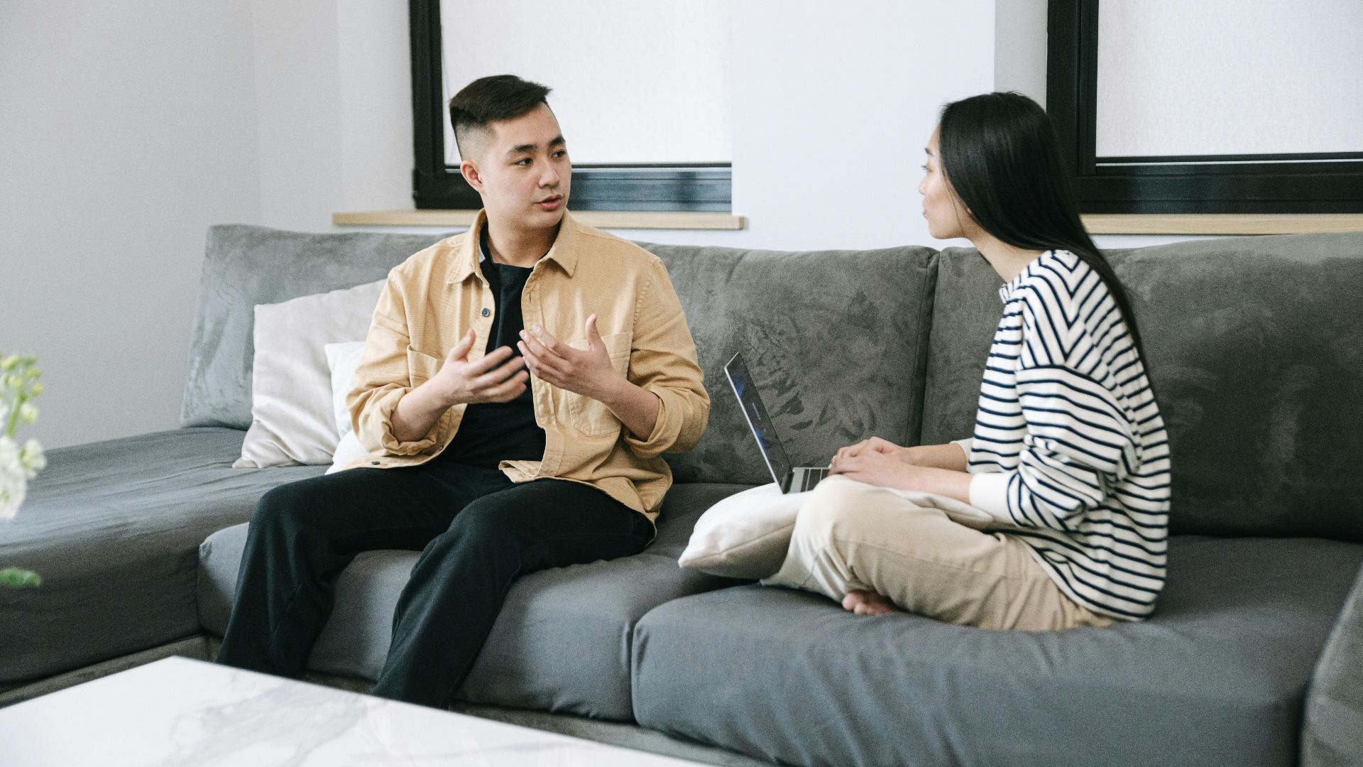 Two young adults engaged in a conversation, sitting on a couch at home.