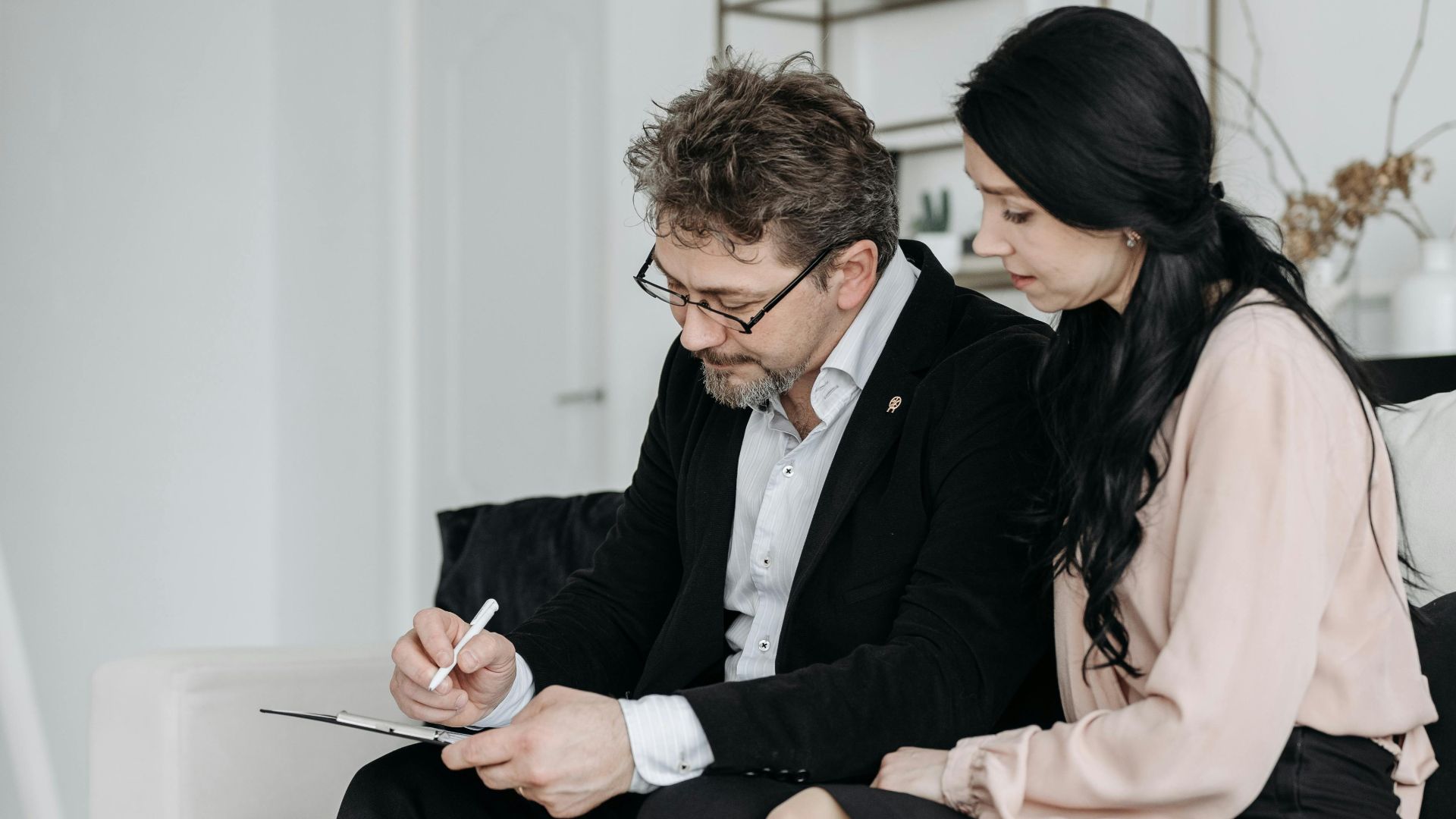 A business man and woman signing documents in a modern home interior.