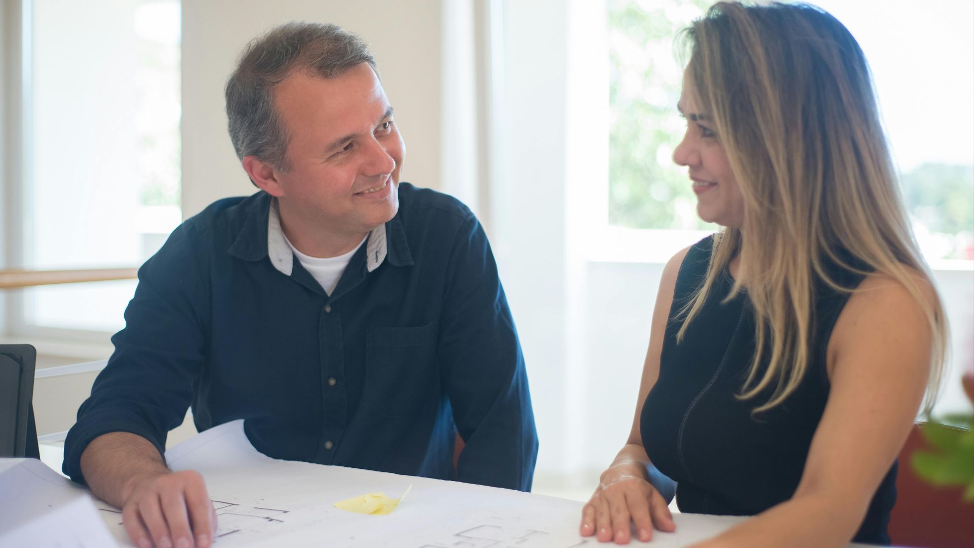 Smiling man and woman reviewing floor plans in a bright office setting.