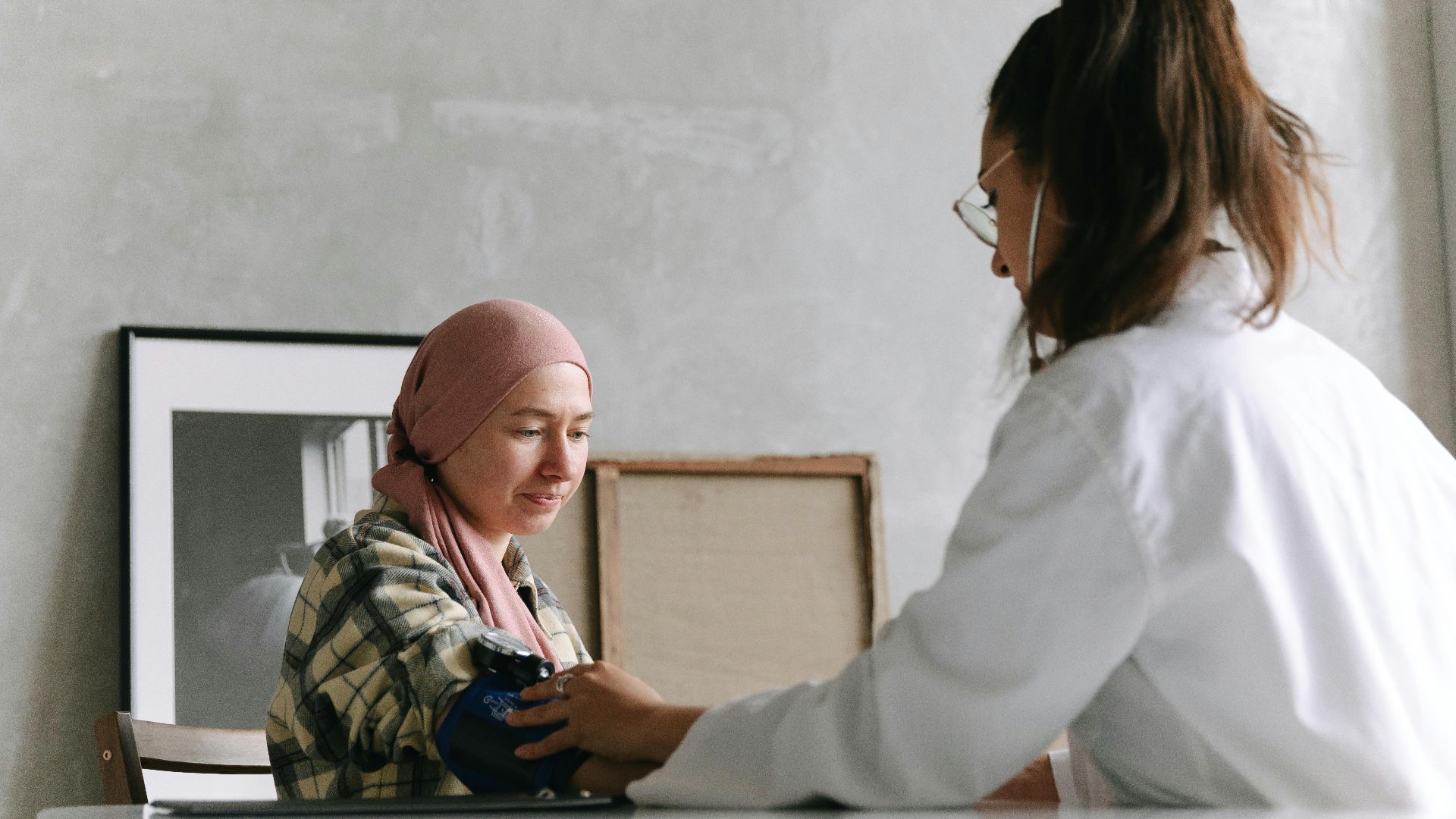 Doctor checks blood pressure of a patient wearing a headscarf indoors, focused on healthcare.