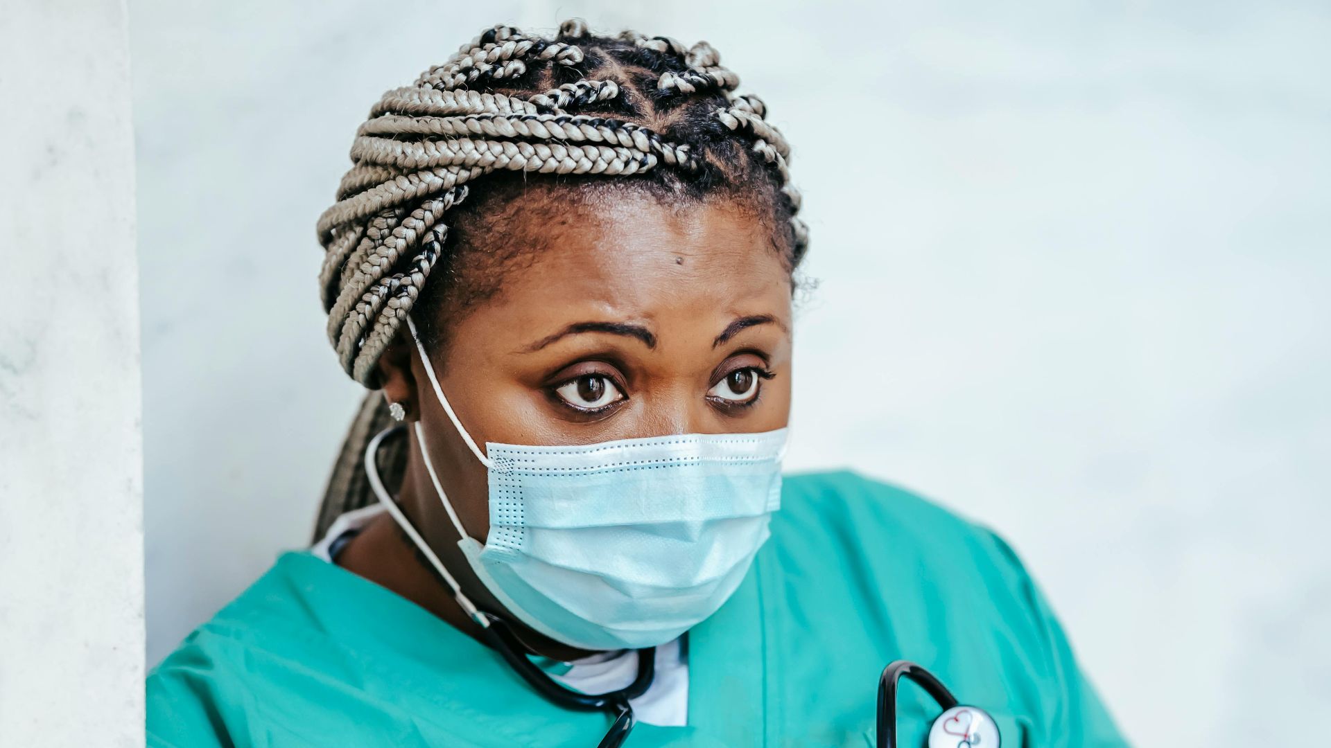 Focused black female medic in medical mask and latex gloves standing with folder while working in clinic