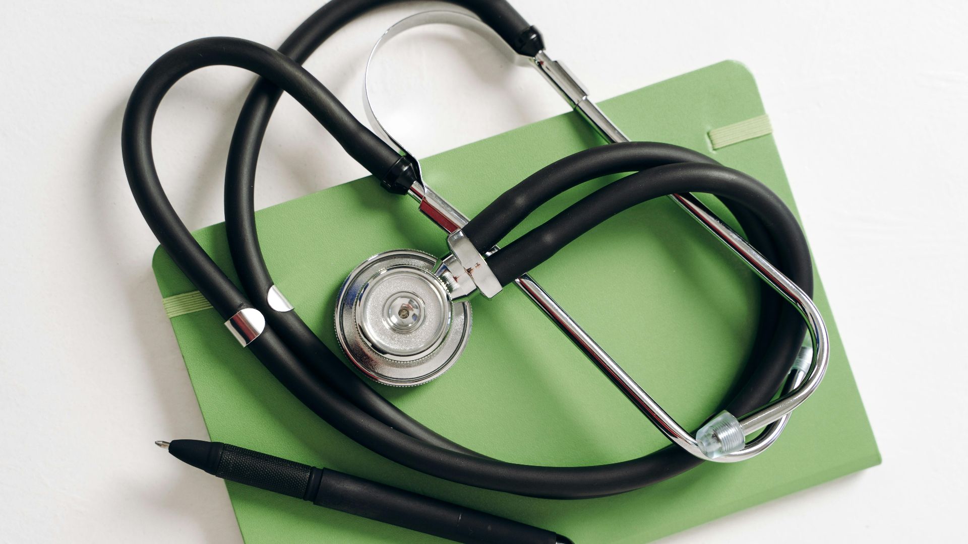 Top view of a stethoscope and pen on a green notepad, ideal for medical and educational themes.