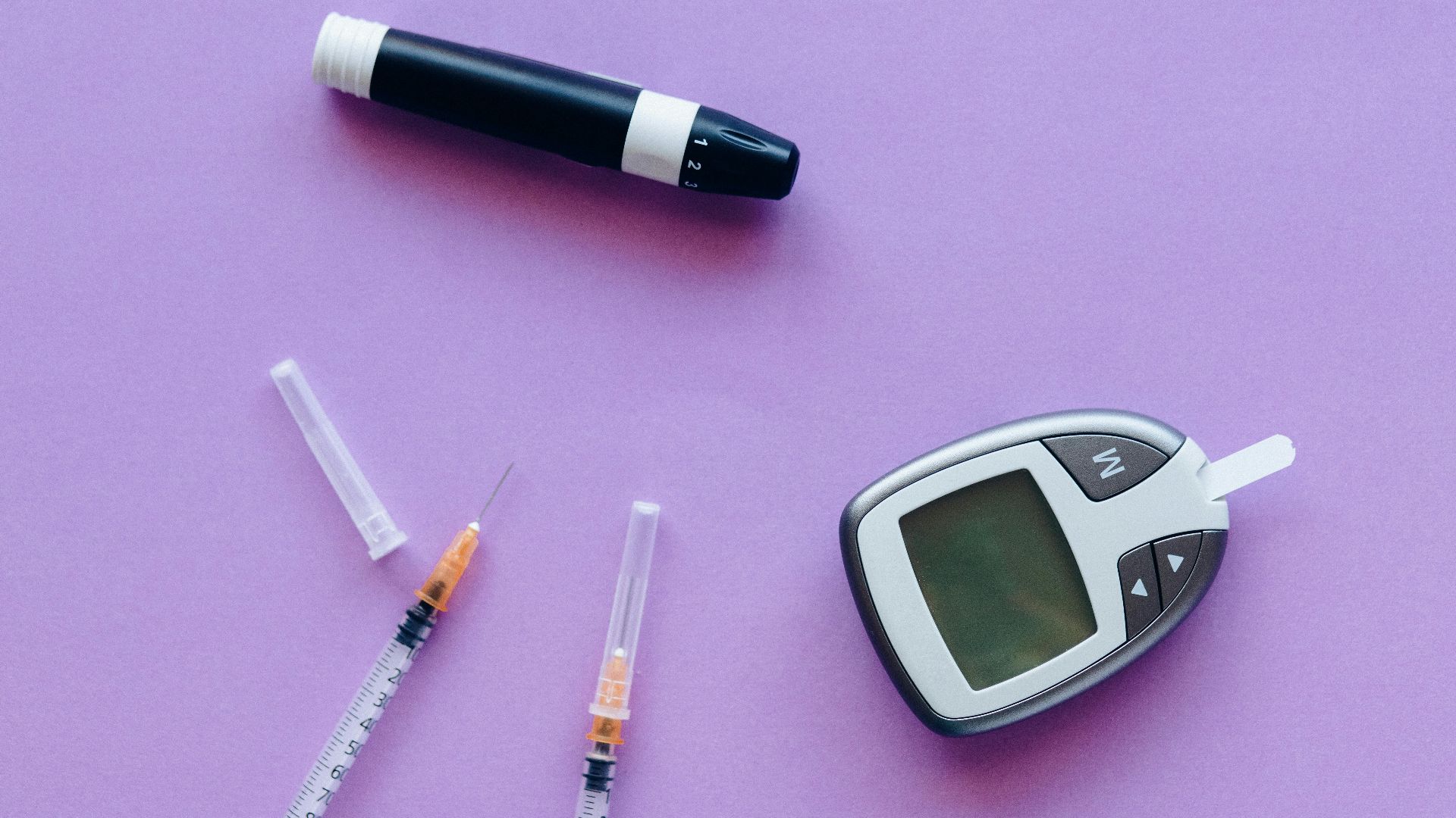 Top view of diabetes management tools including glucose meter and insulin syringes on purple background.