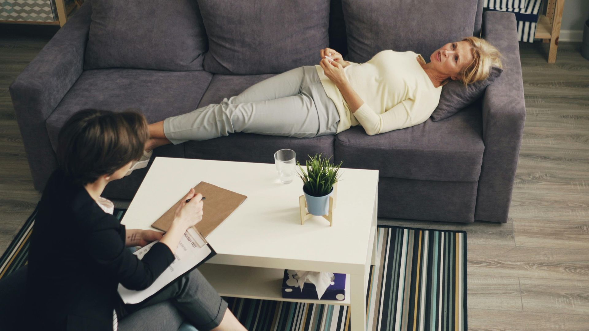 A therapist consulting with a patient reclining on a sofa in an office setting.