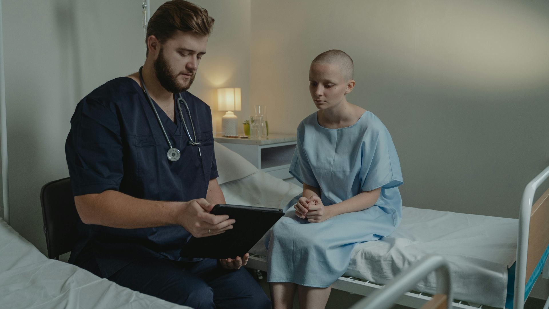 A doctor in a hospital ward consulting a patient with a digital tablet.