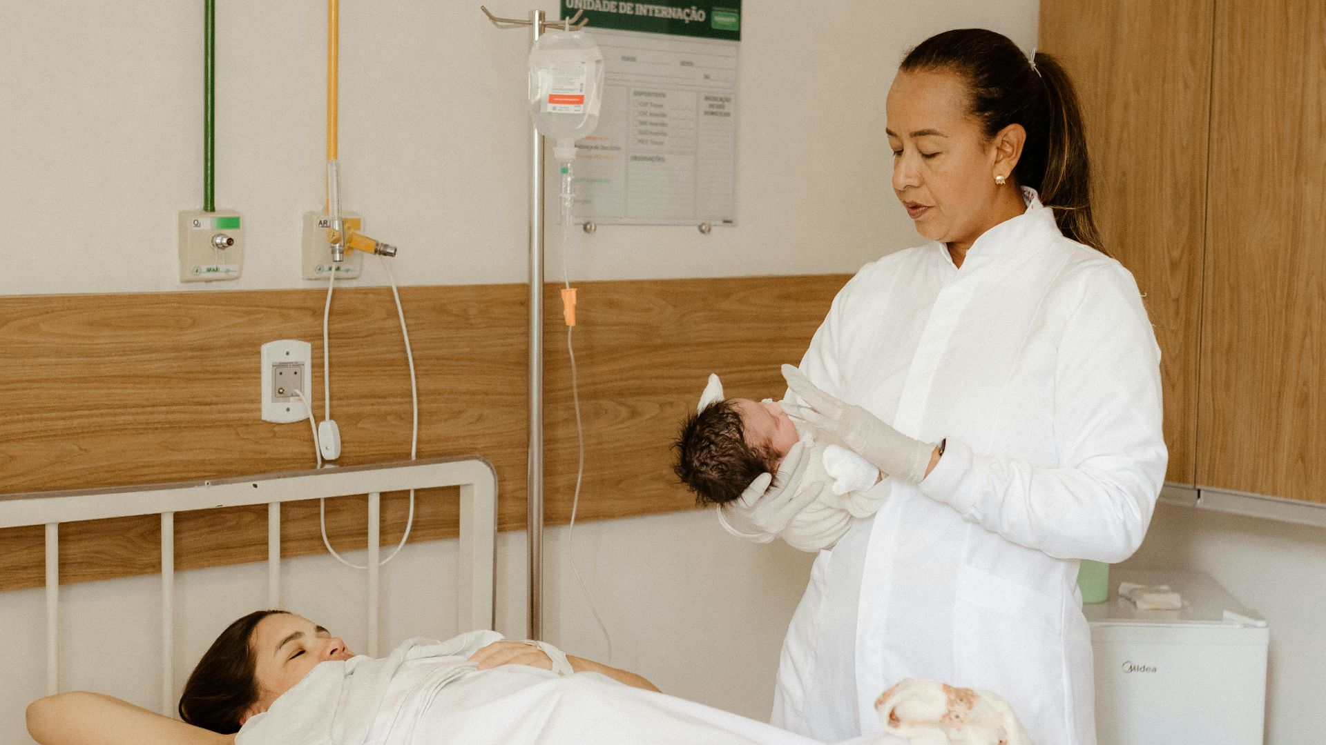 New mother and newborn in hospital room with medical staff attending.