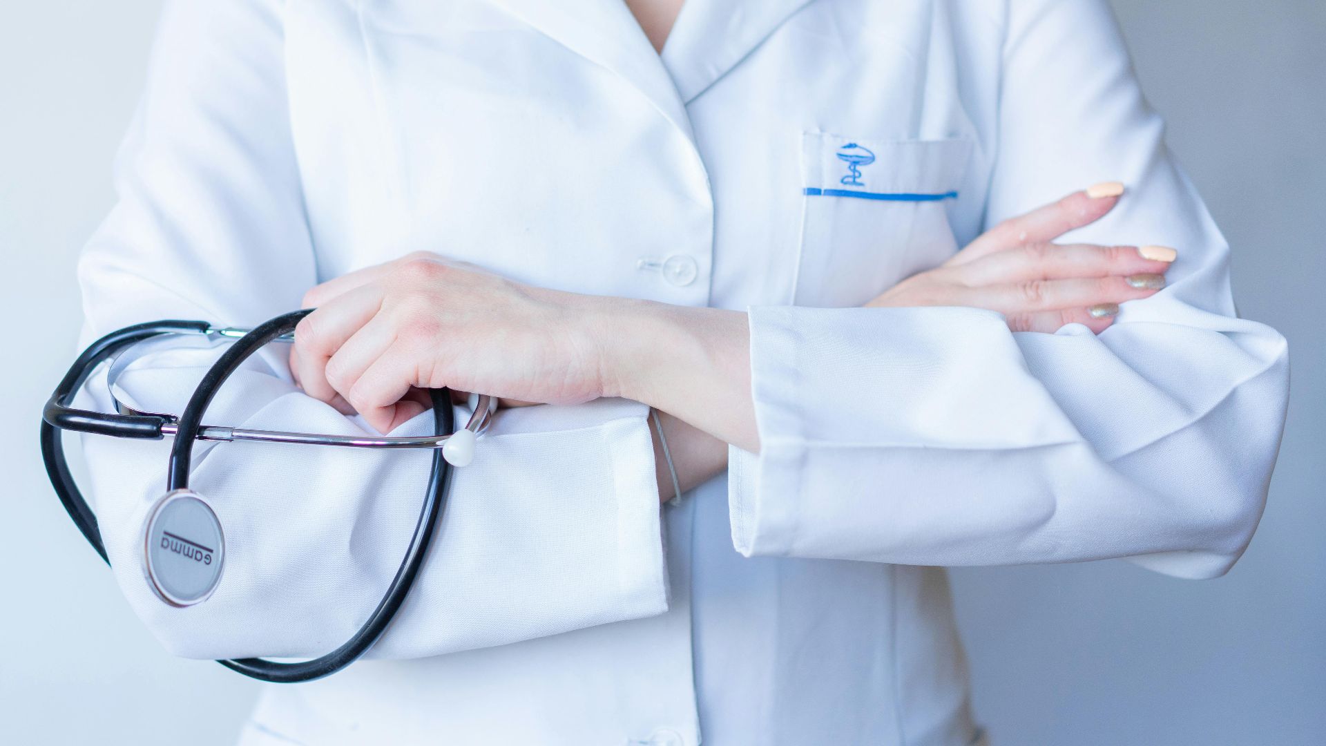 A close-up image of a doctor in a white coat with a stethoscope and arms crossed.